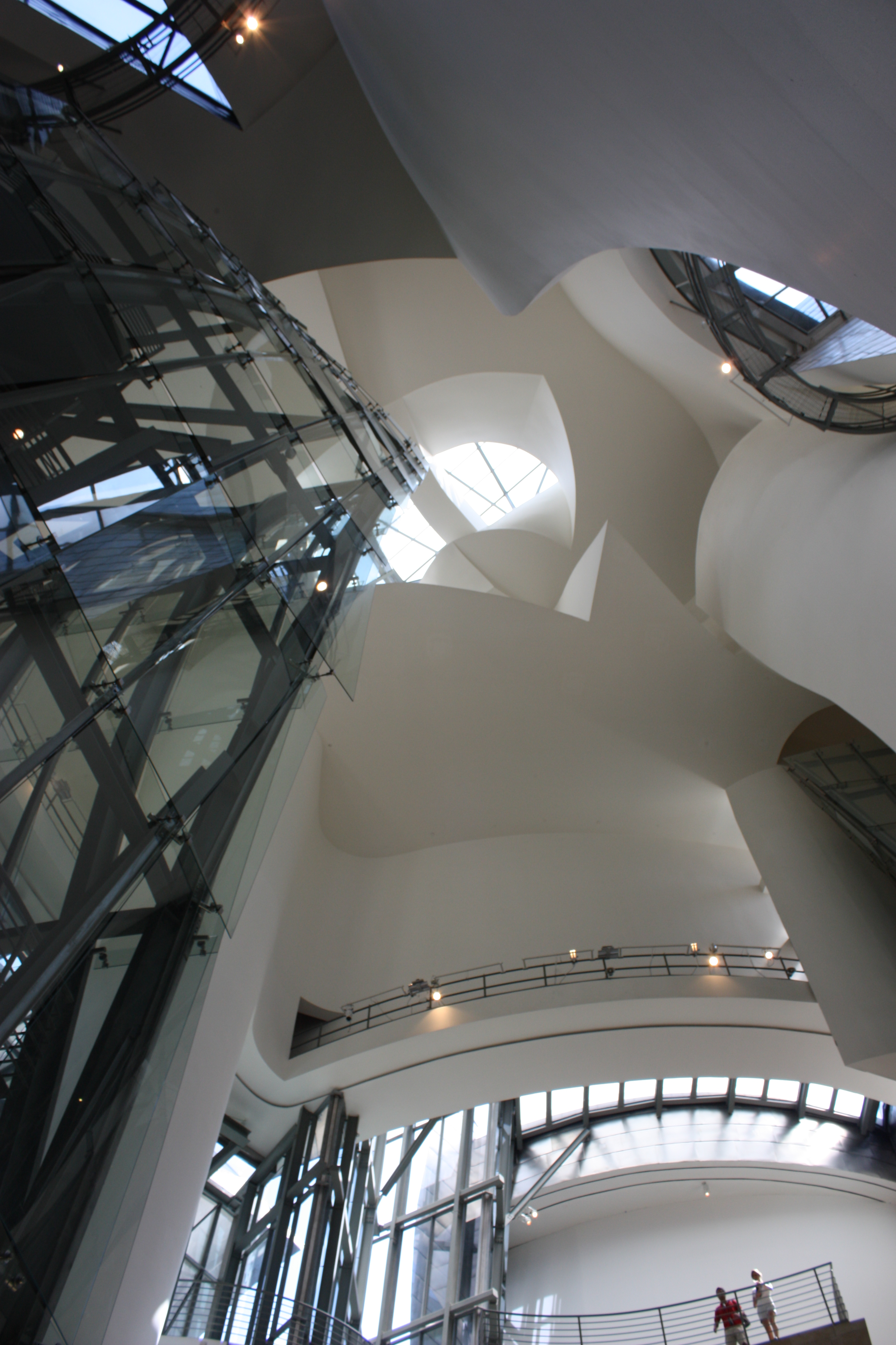 Interior view of the Guggenheim Museum Bilbao, showcasing its unique architecture with curved white walls, glass elevator, and skylights.