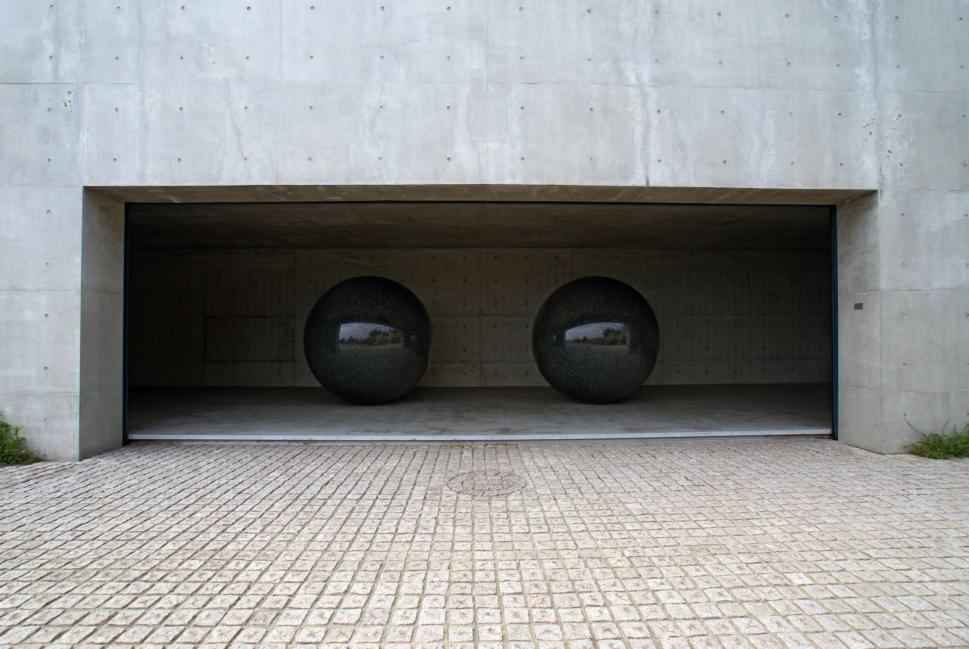 Two large, dark, polished spherical sculptures displayed inside a modern concrete building at Benesse House on Naoshima art island, Japan.