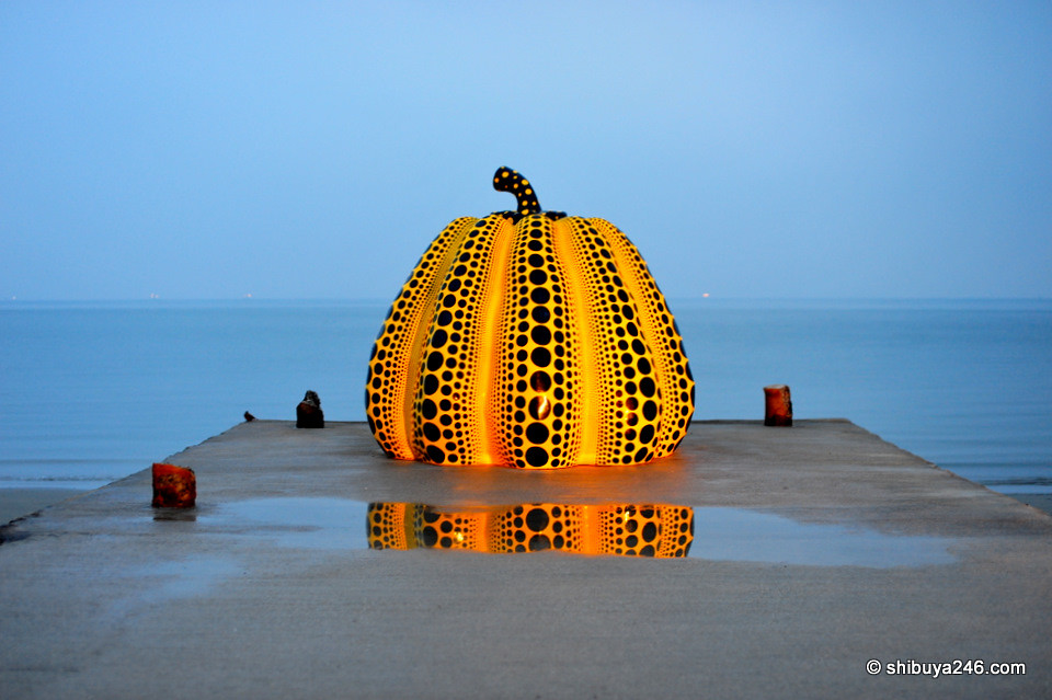 Naoshima's iconic yellow pumpkin sculpture by Yayoi Kusama on a pier at dusk, with its reflection in the water.