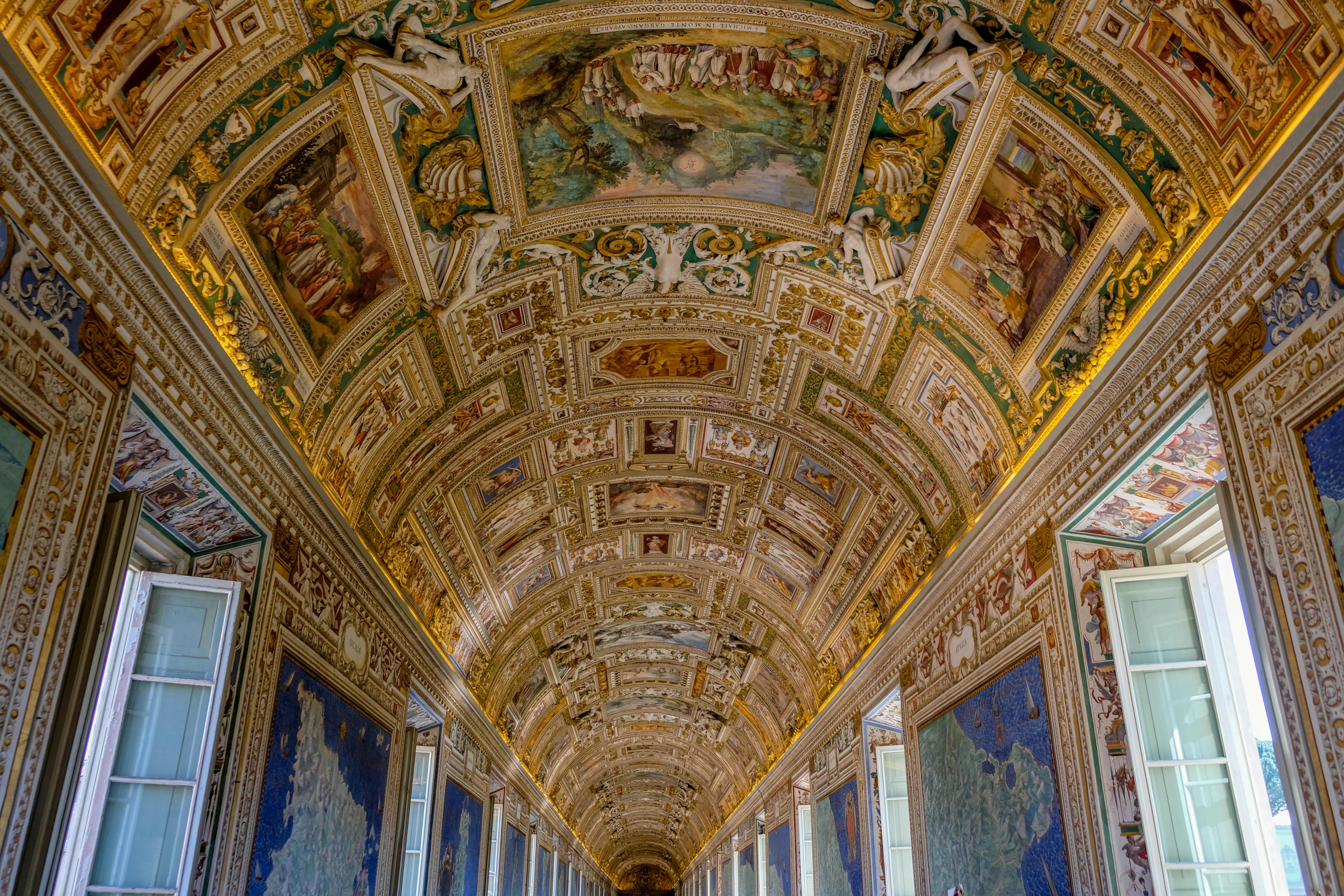The ornate painted ceiling of the Gallery Corridor in the Vatican Museums, featuring intricate frescoes and golden decorations.