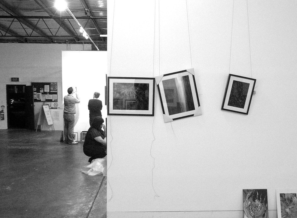 Curated artworks on display in a gallery with multiple framed pieces and exhibition context boards visible in the background.