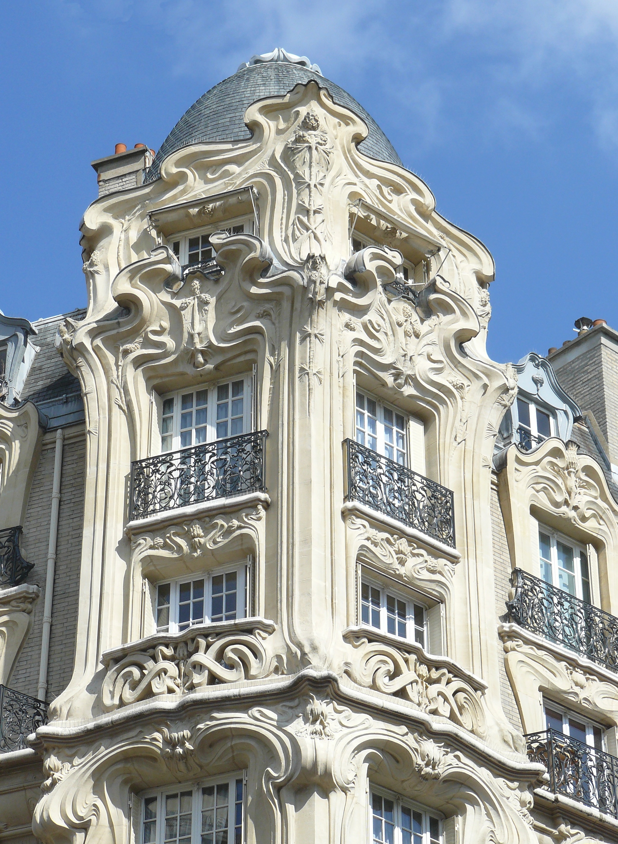 Art Nouveau building facade detail with ornate sculptures and a dome in Paris.