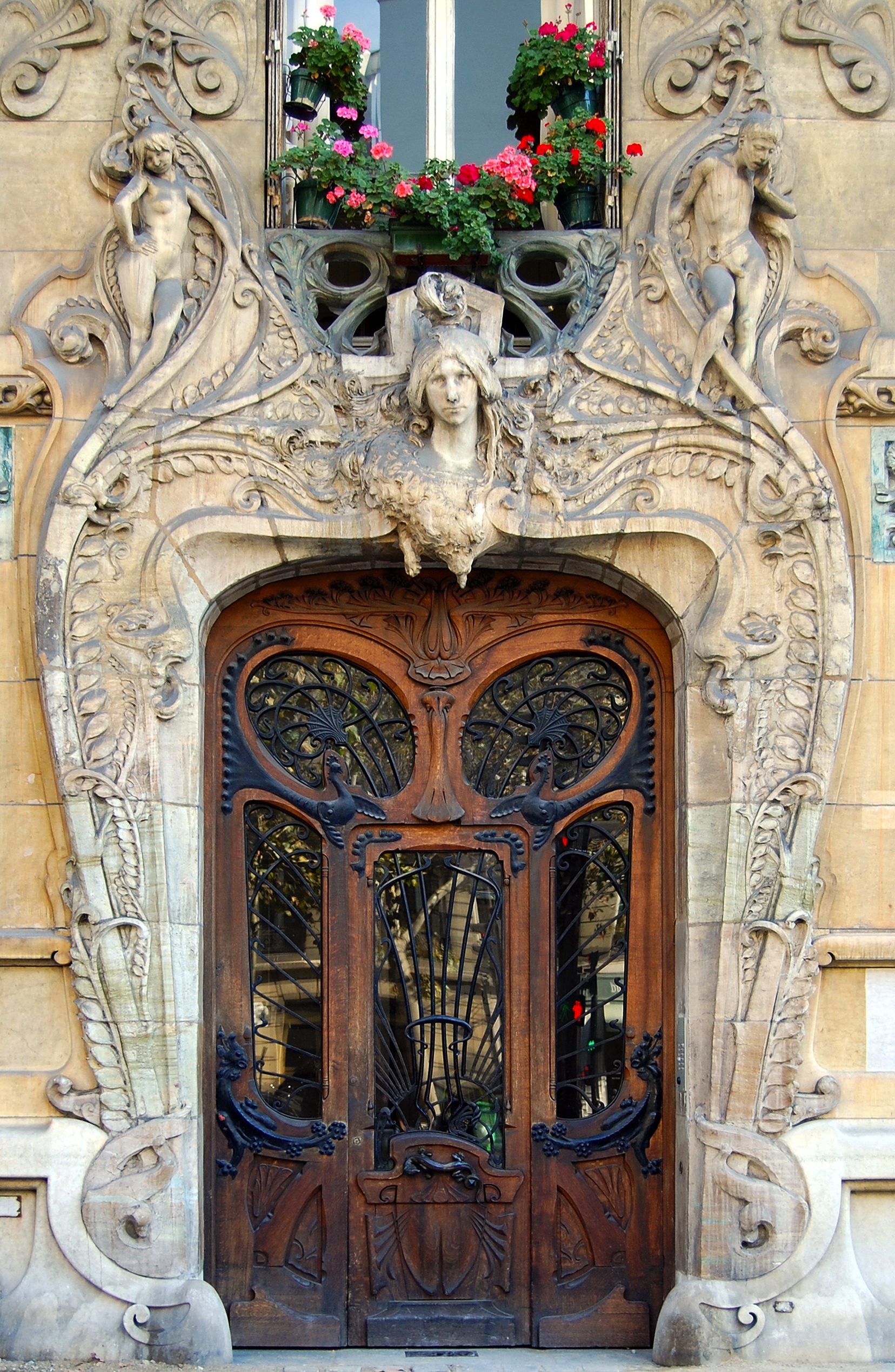 Ornate Art Nouveau doorway in Paris with sculpted figures, floral motifs, and a wooden door with wrought iron details.
