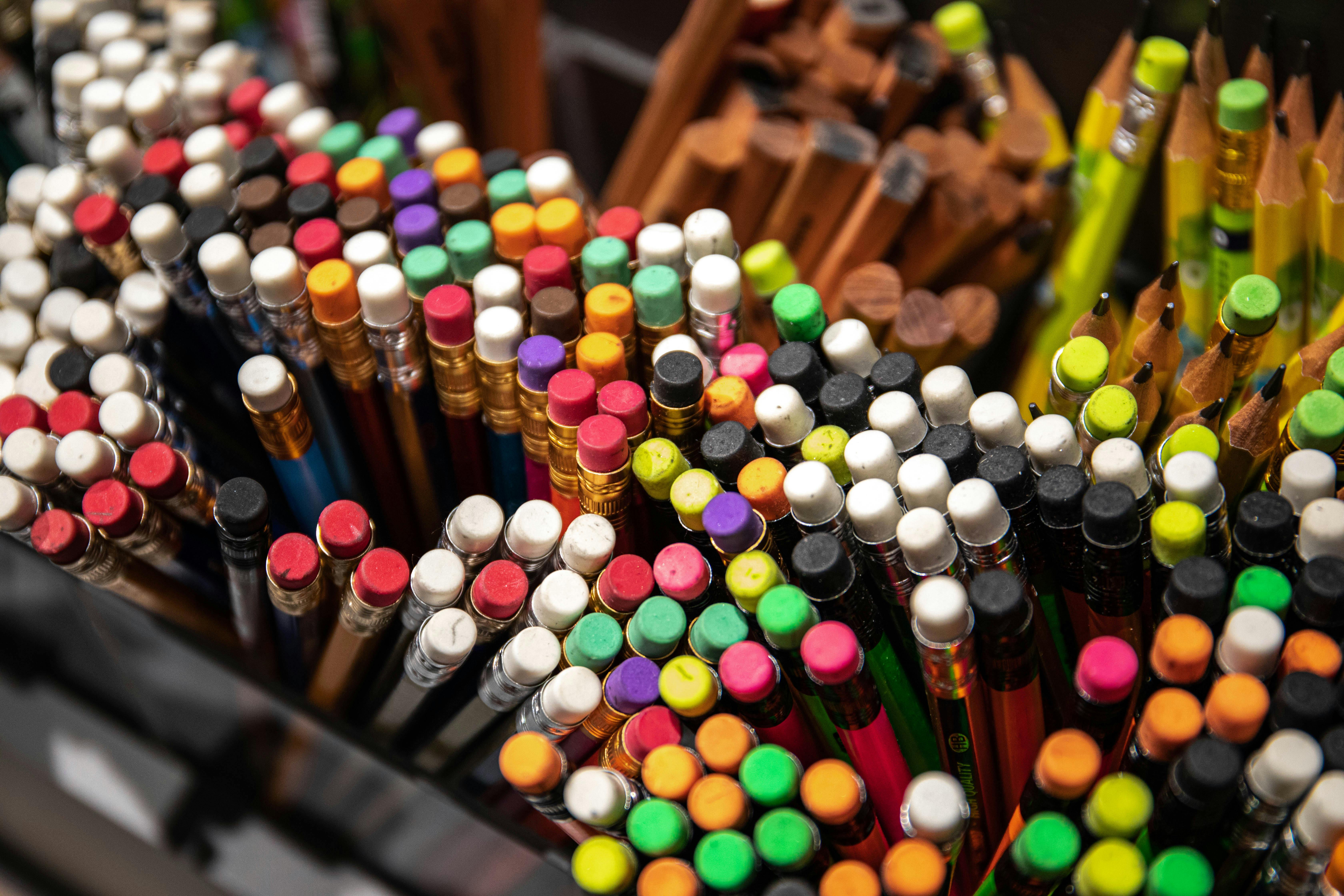 A close-up view of a variety of colored pencils with erasers in a box, showcasing a vibrant collection of art supplies.