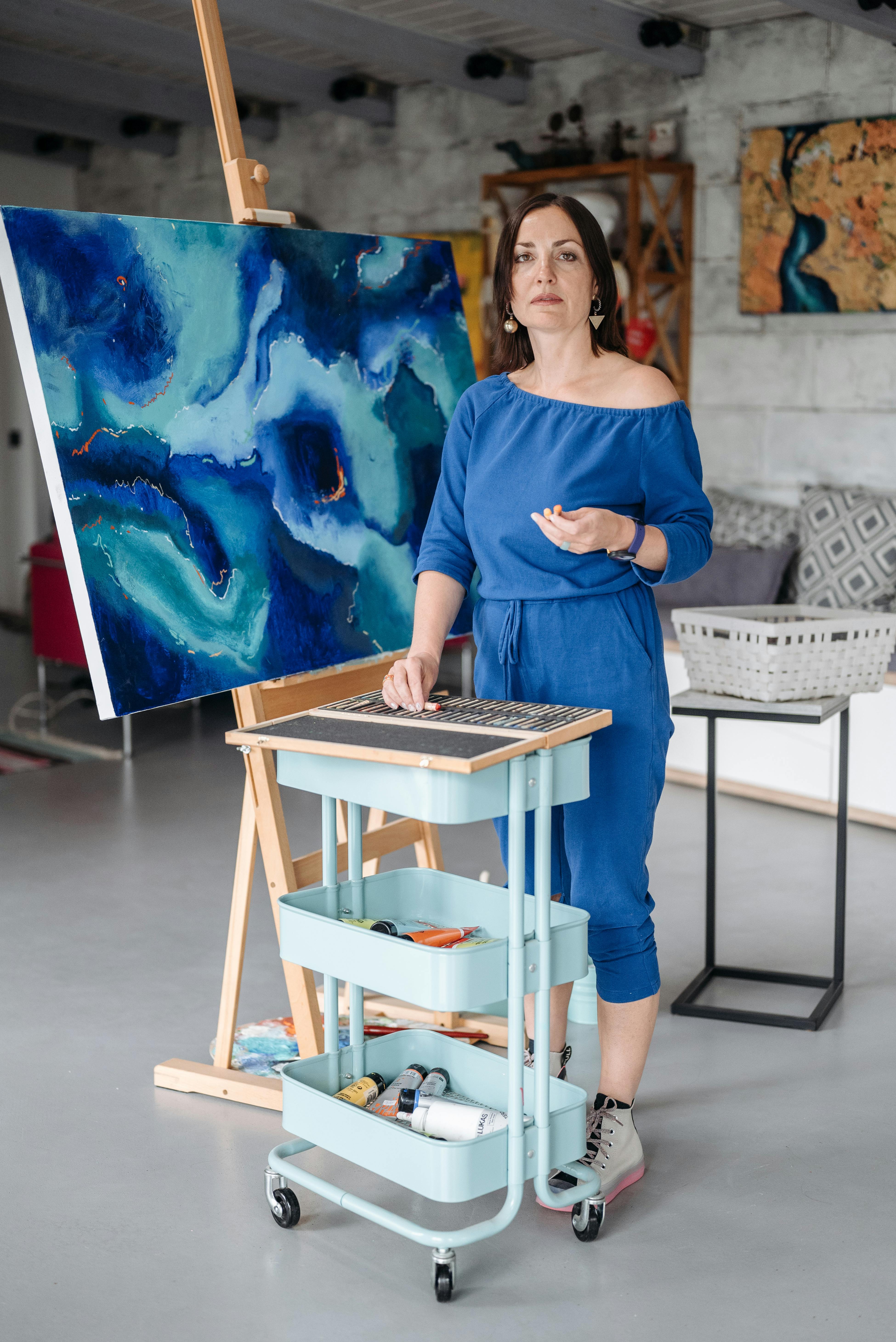 Woman standing next to a painting on an easel in an art studio.