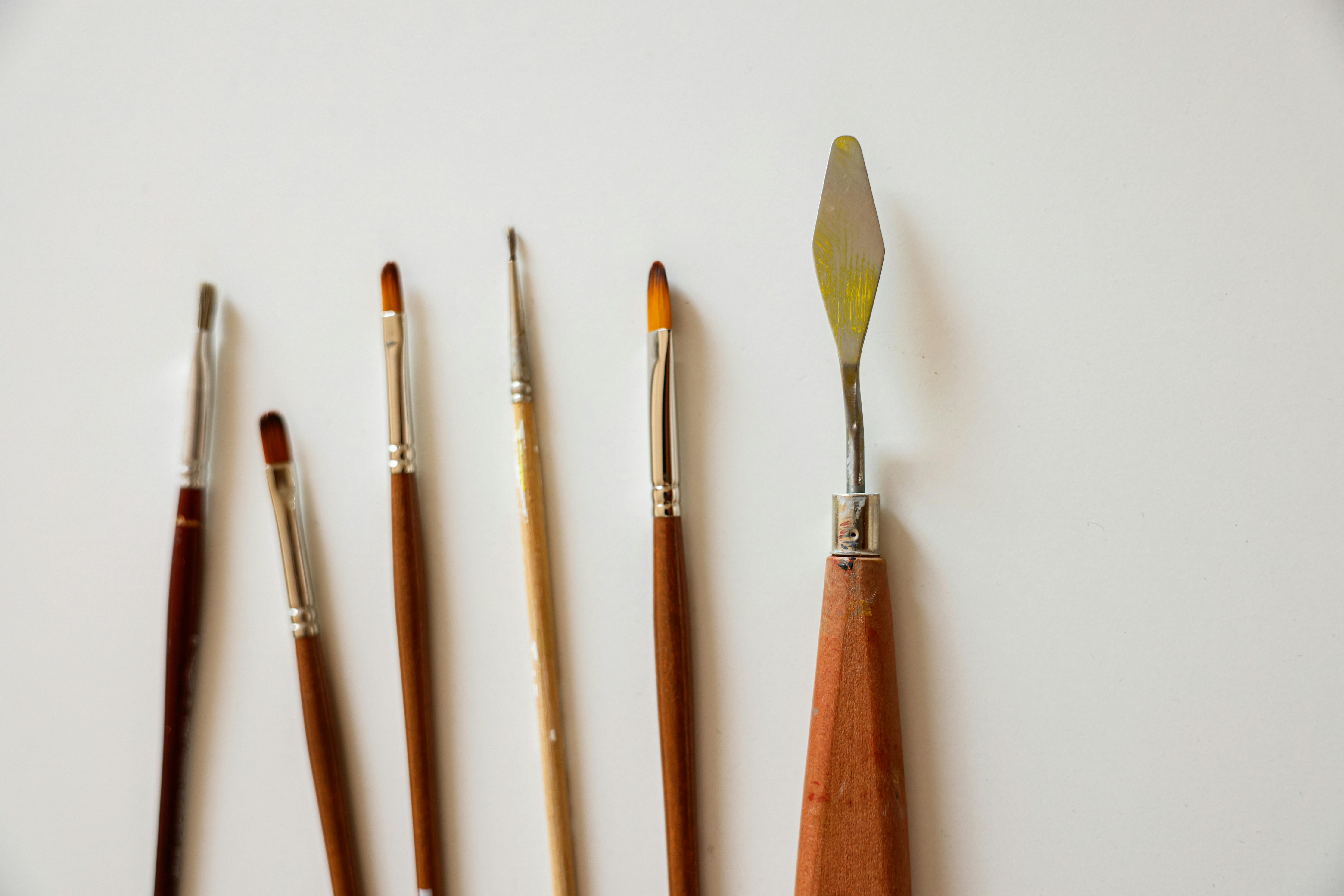 A collection of paint brushes and a palette knife arranged on a white surface, ready for abstract painting.