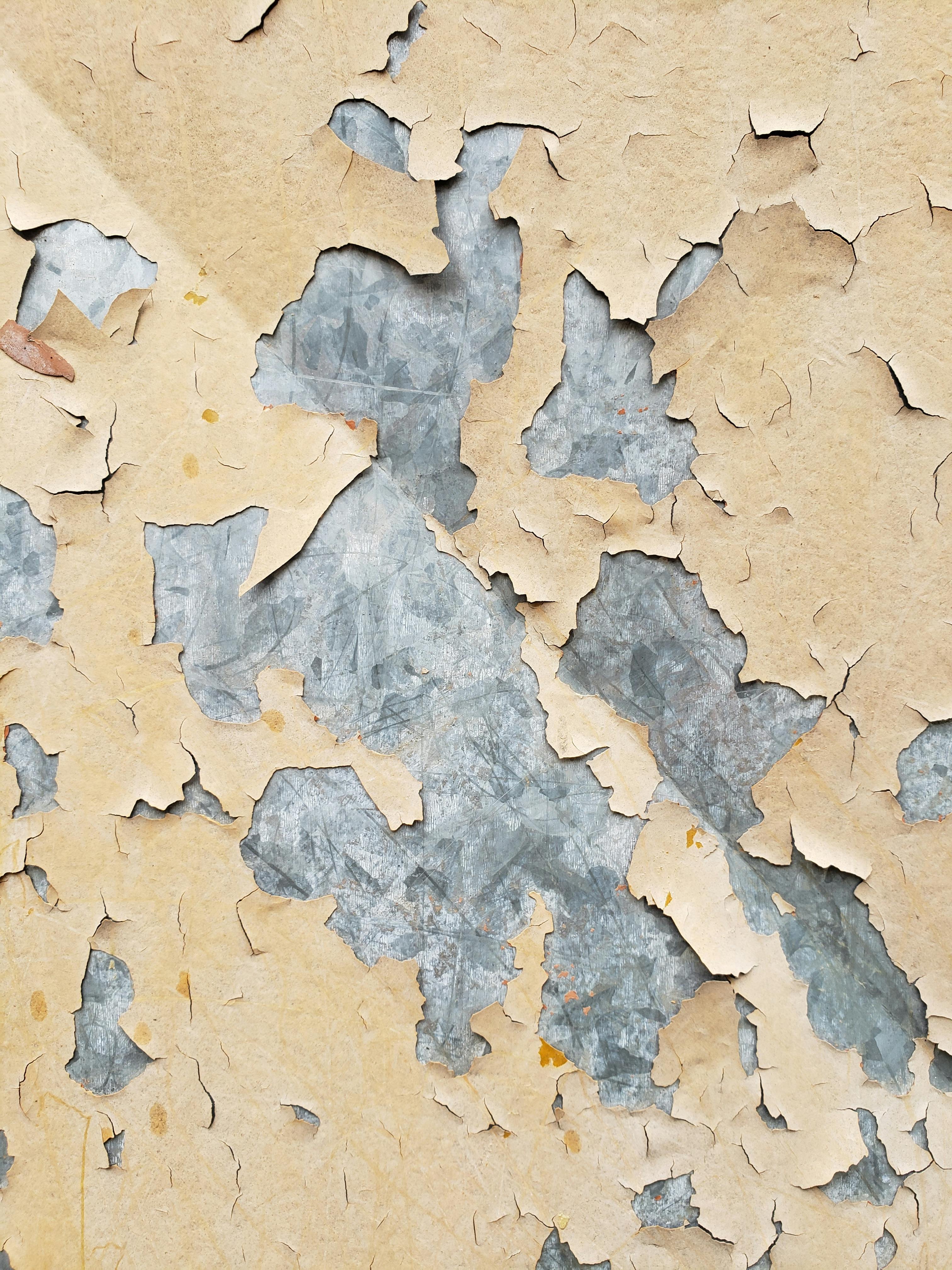 Close-up of cracked and peeling beige paint revealing a textured grey metal surface underneath.