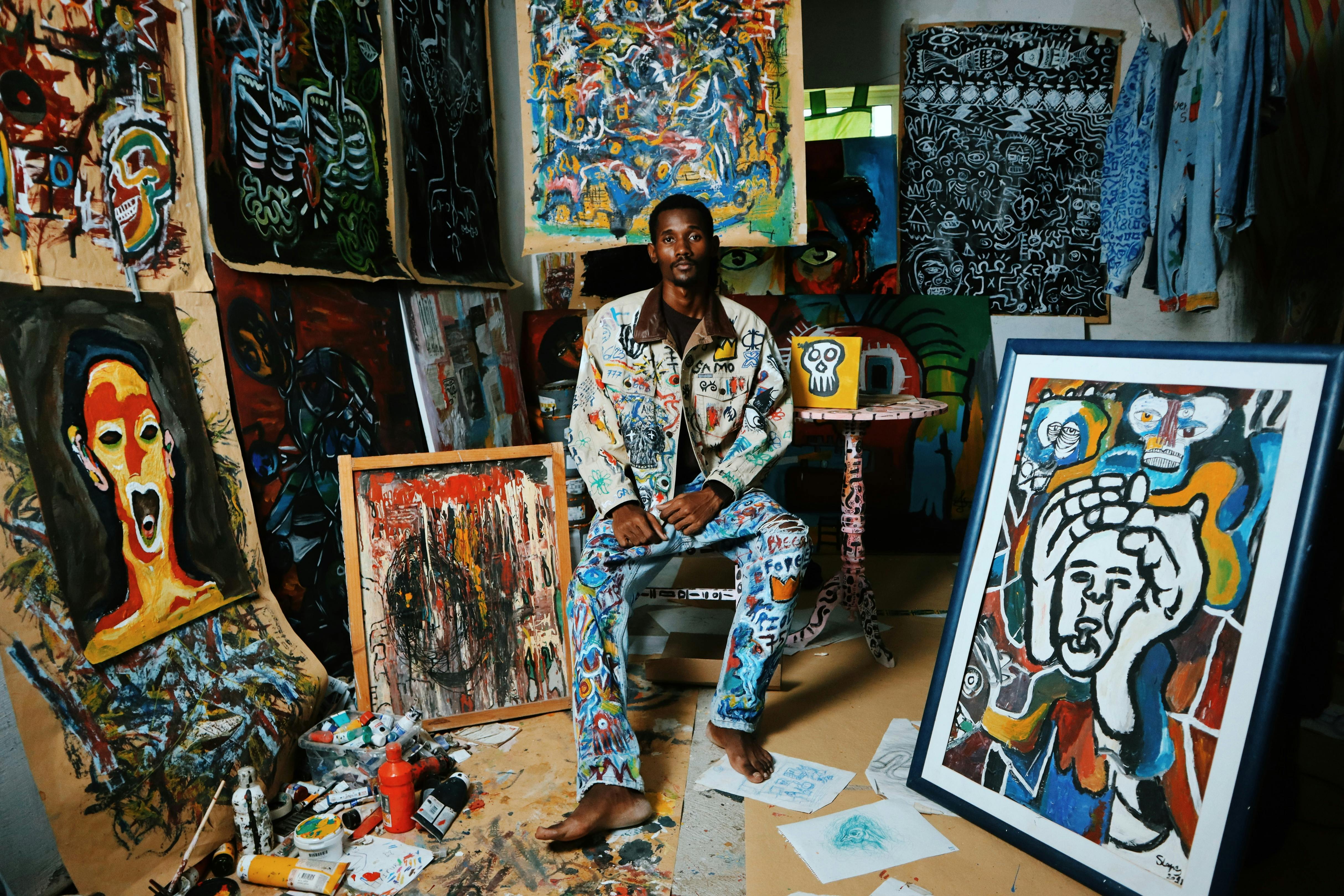 Artist surrounded by paintings in a creative studio environment with art supplies, showcasing the process of art creation for art buying considerations.