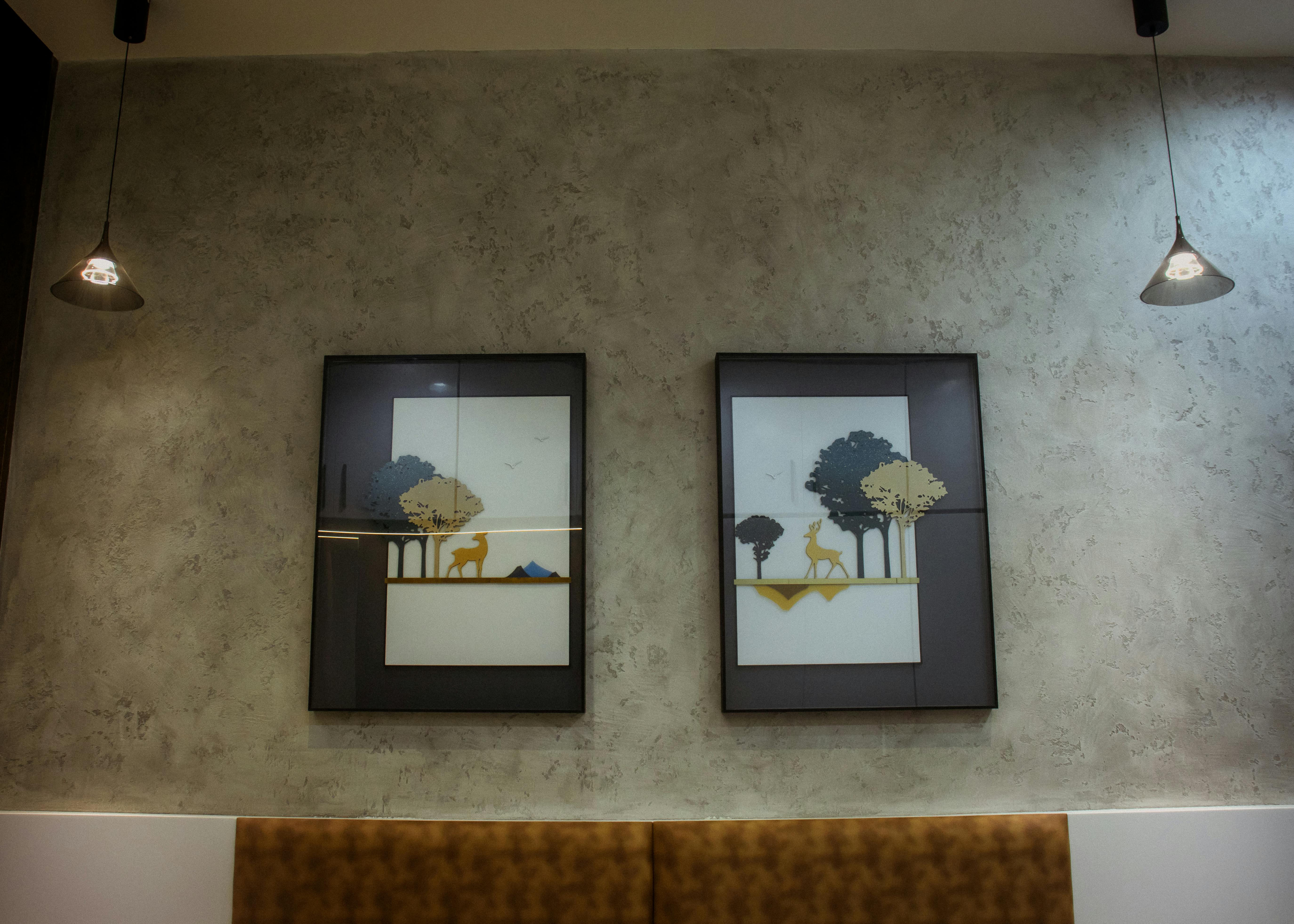 Two contemporary paintings on a textured wall featuring deer and bird silhouettes, with warm lighting and natural elements - free stock photo for interior decorating ideas