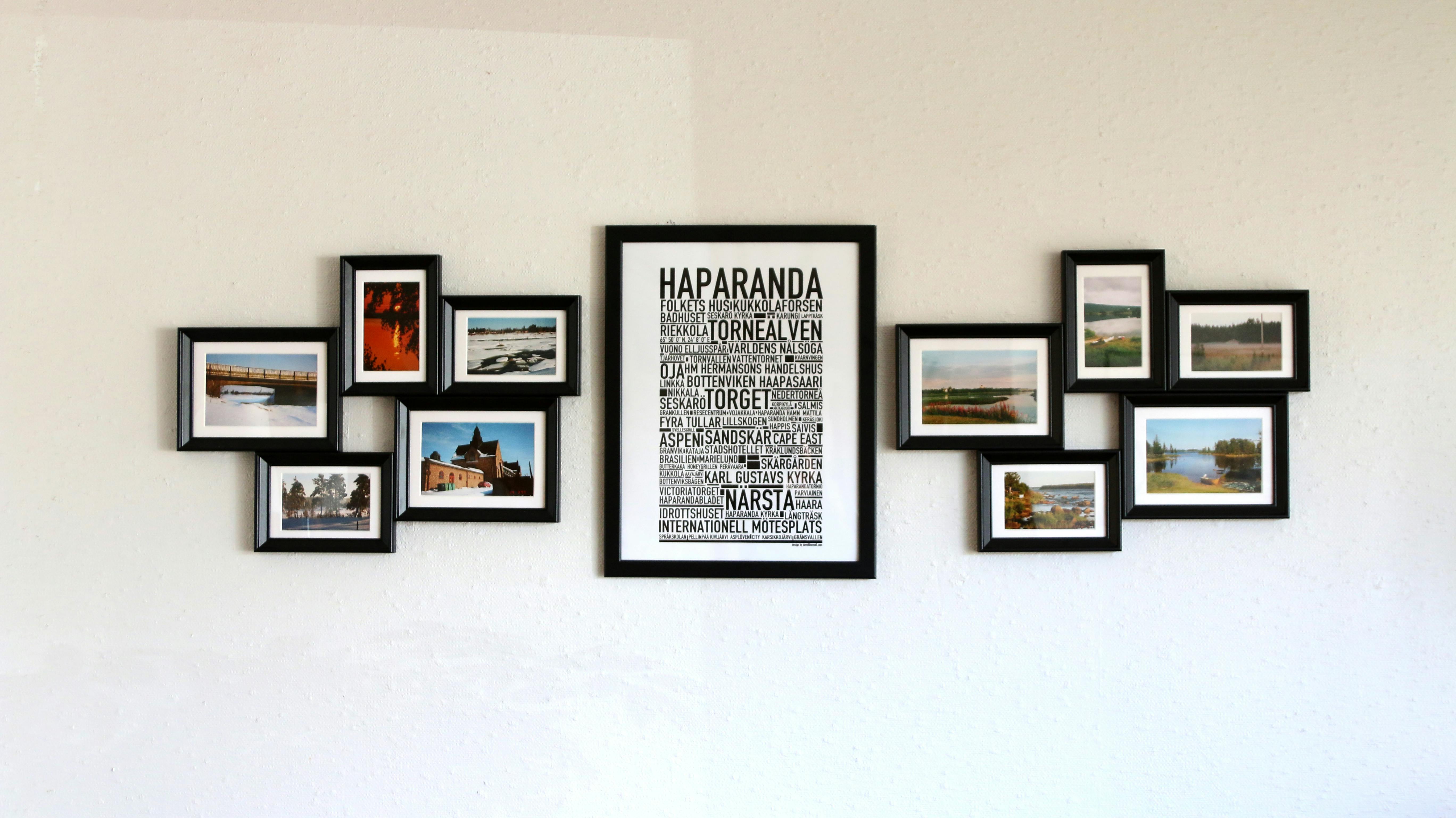 Framed photos of landscapes and urban scenes arranged symmetrically on a white wall, featuring HAPARANDA and TORGET text elements.