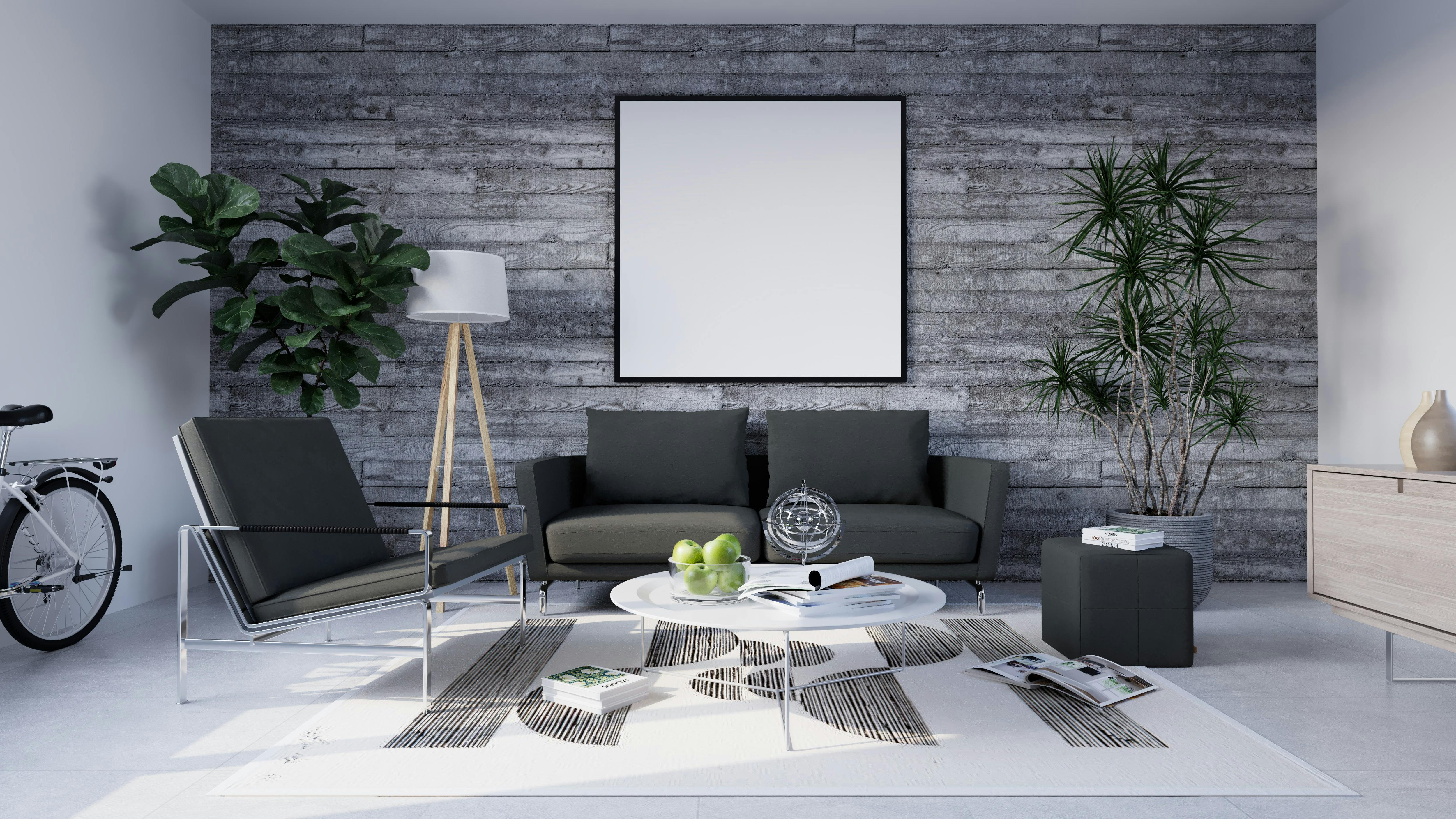 Modern living room with a concrete wall featuring a large blank picture frame, dark grey sofa, armchair, and a round coffee table with books and decorative items.