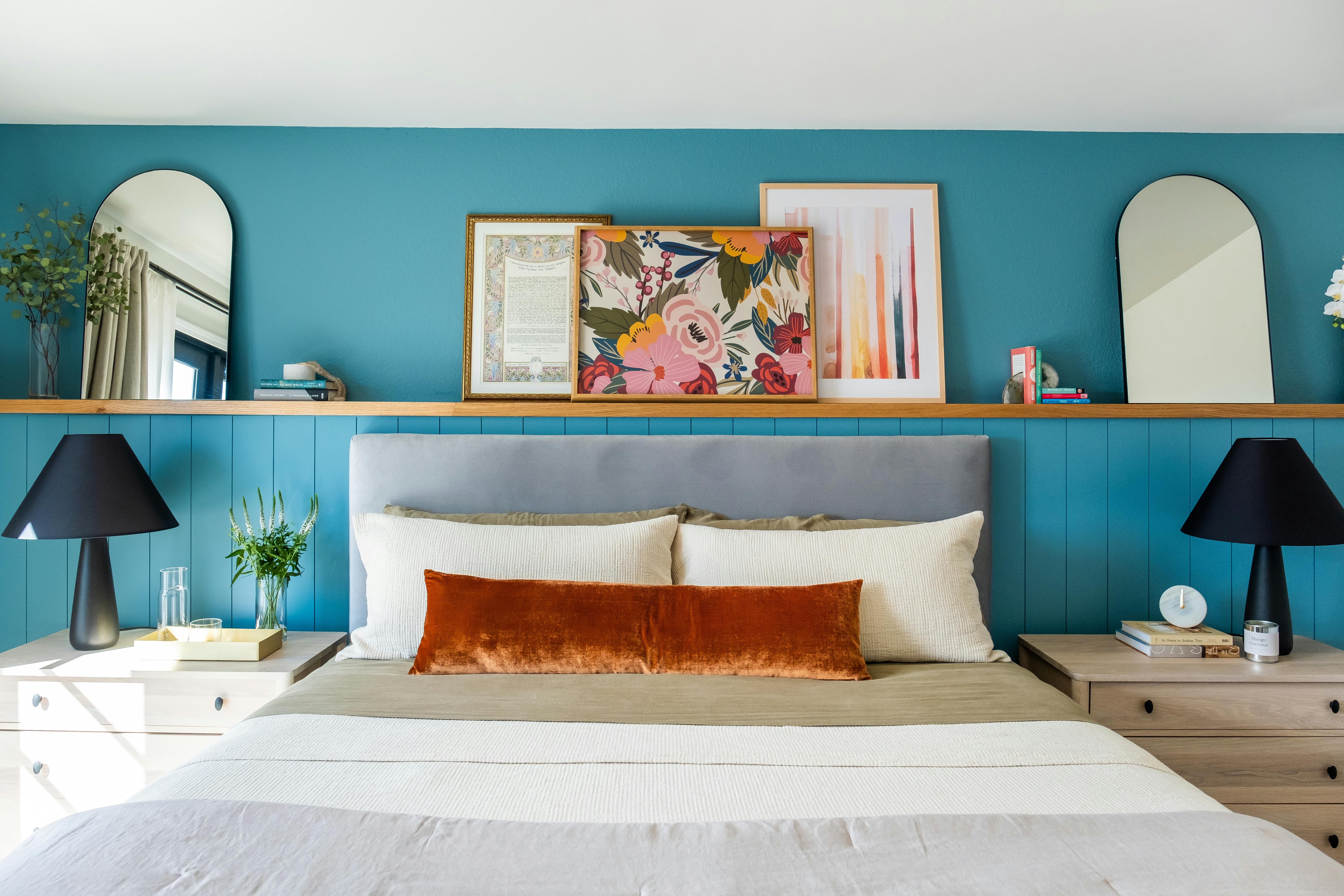 Bedroom interior with teal walls, a grey headboard, and curated wall art above the bed.