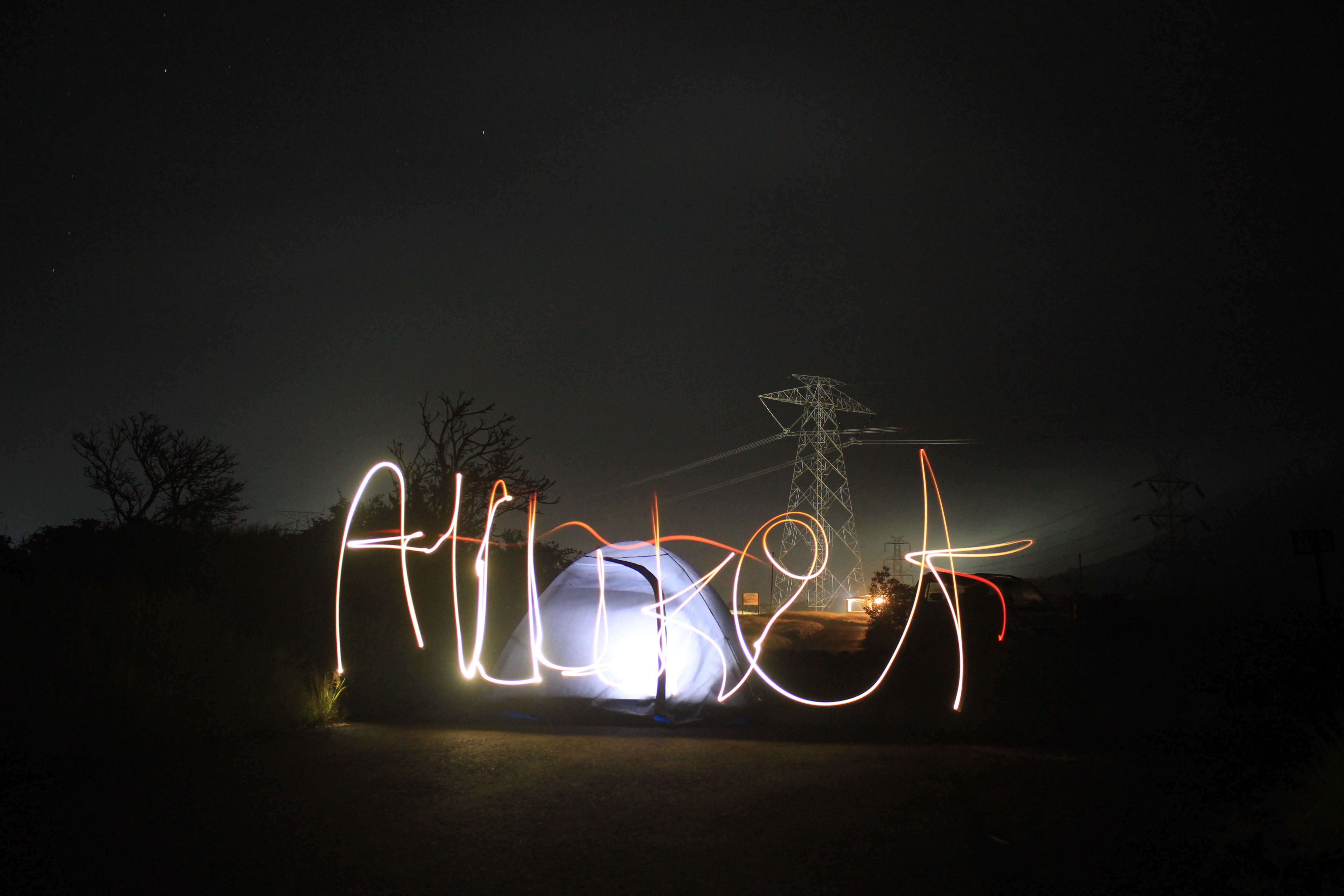 Light painting of the word 'Allure' in front of a glowing tent at night, with power lines and a pylon in the background.