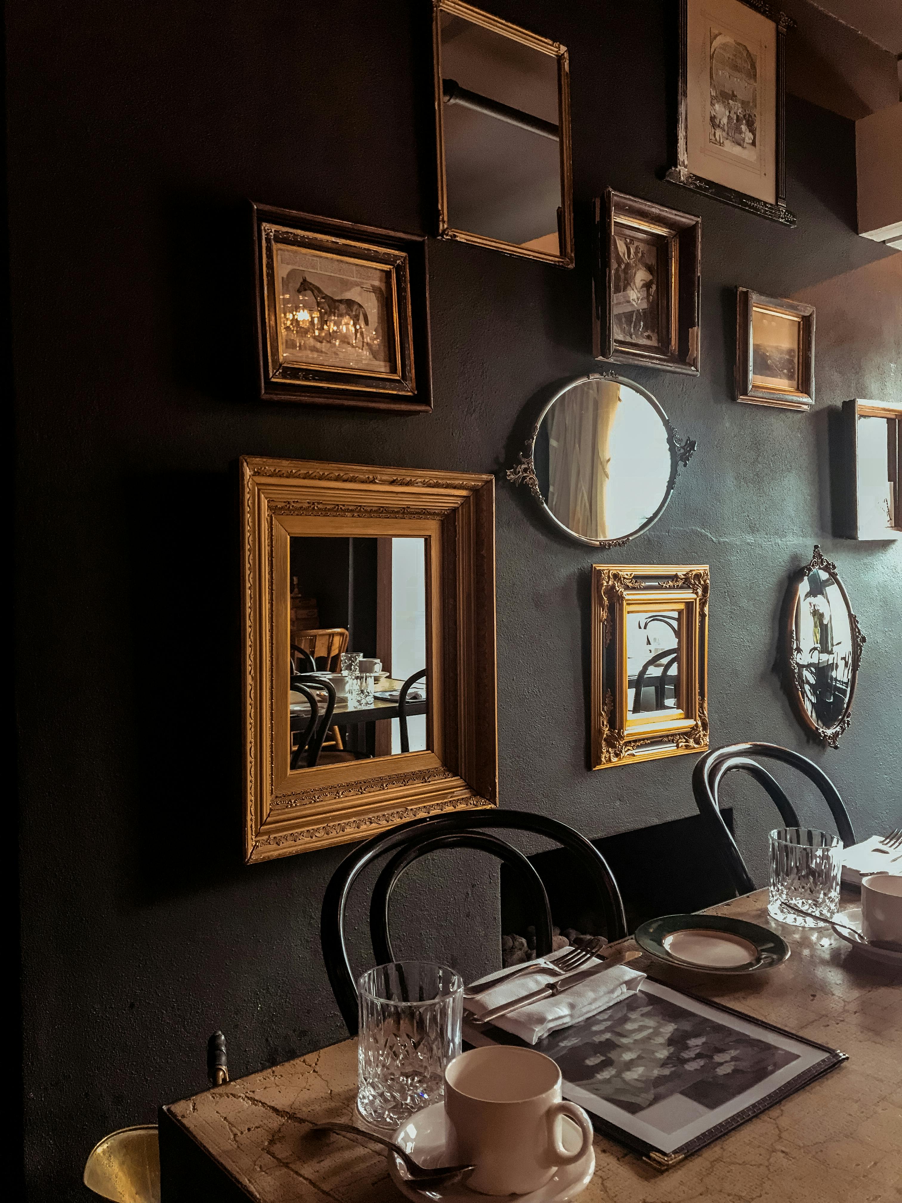 Collection of framed mirrors and art pieces arranged on a dark, textured wall above a dining table.
