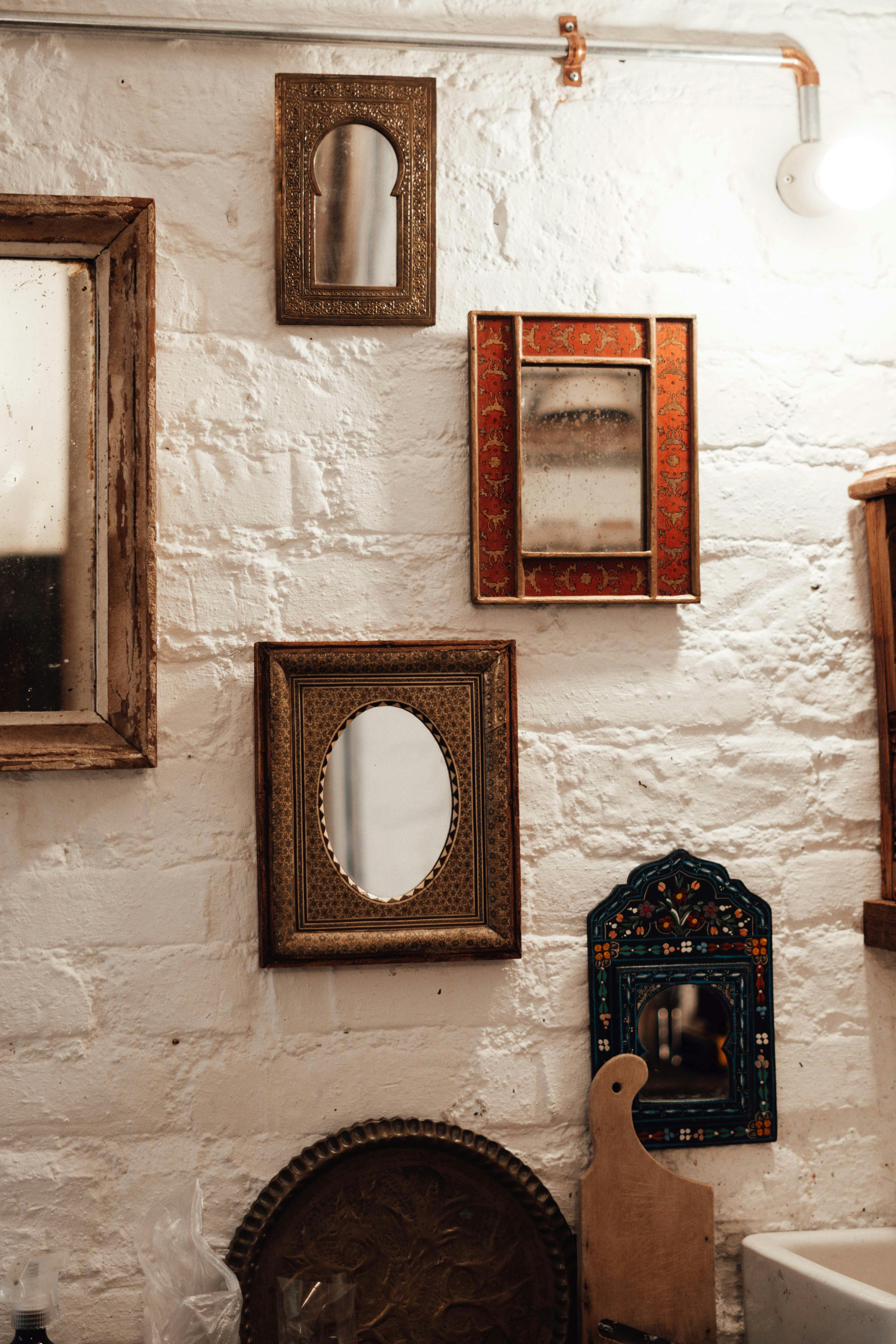 Collection of retro mirrors with ornate decorative frames arranged on a textured white brick wall, featuring gold, red, and blue frames.