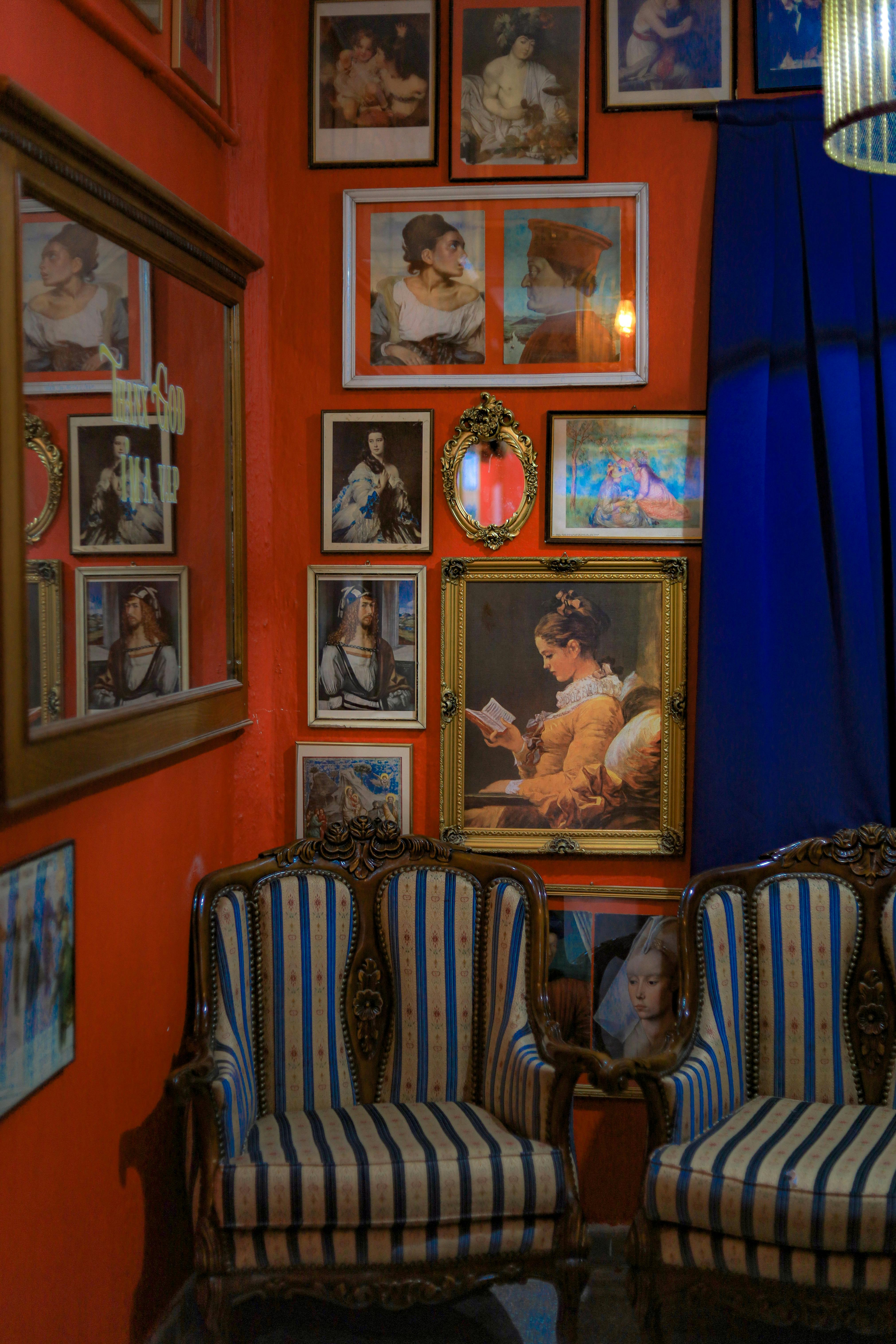 Ornate striped armchairs placed in front of a vibrant red wall adorned with a collection of framed art and decorative mirrors.