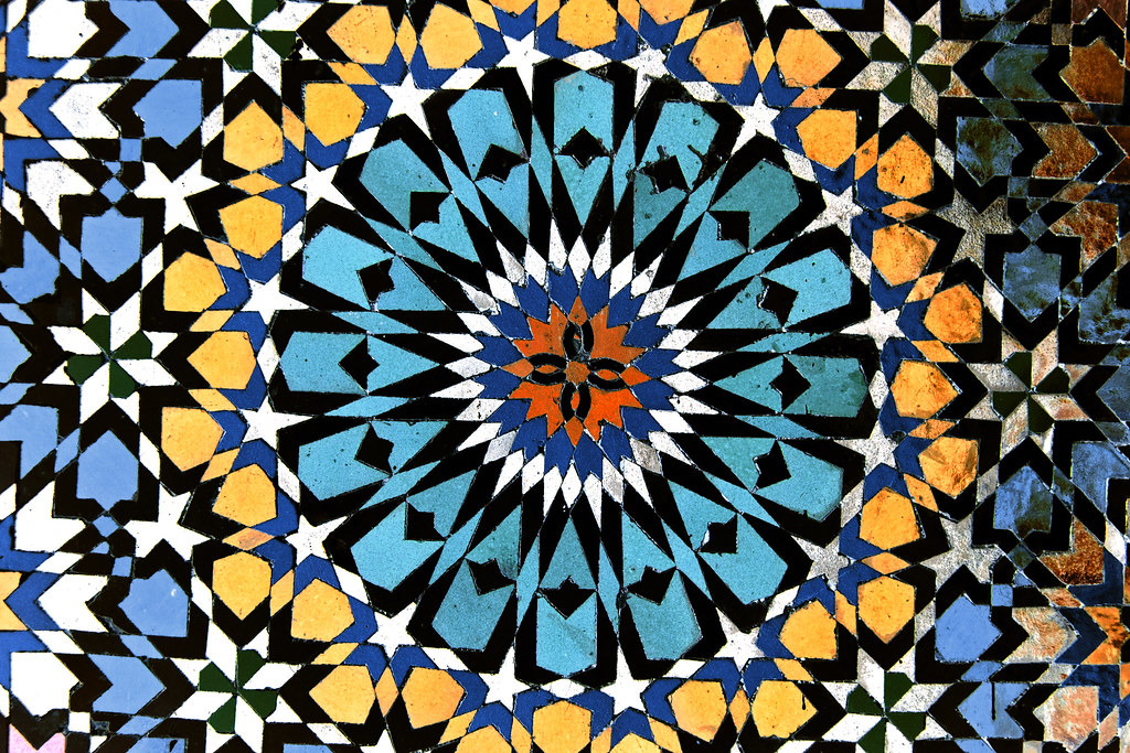 Intricate geometric Islamic tile pattern from Morocco, featuring blue, yellow, and orange stars and polygons.