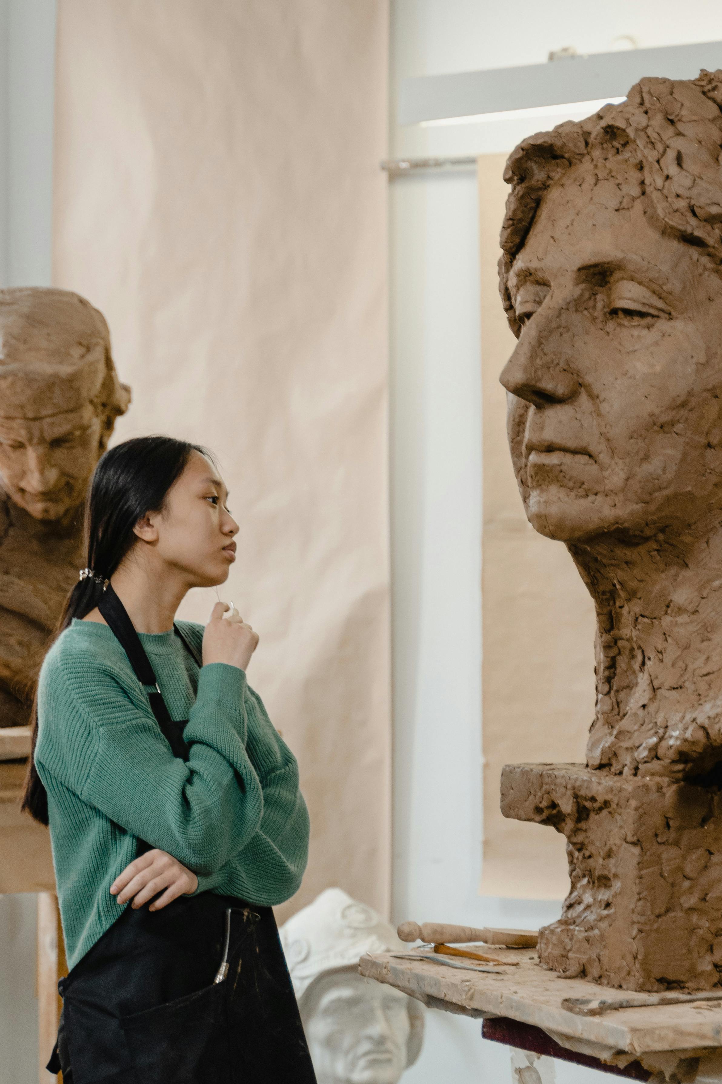 A female sculptor intently examining a clay sculpture during the creative process in an art studio.