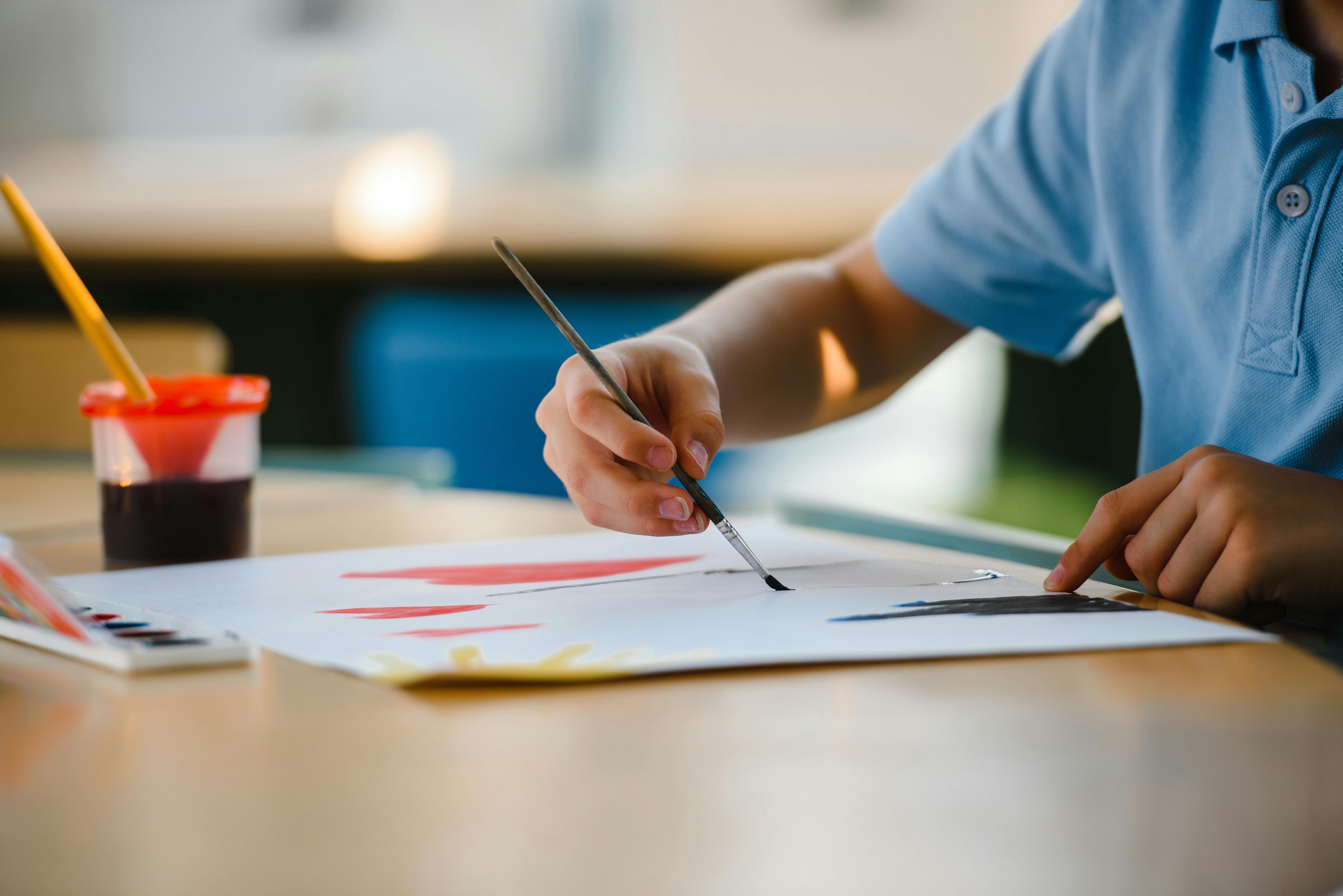 Close-up of a child's hands painting with watercolors on white paper.