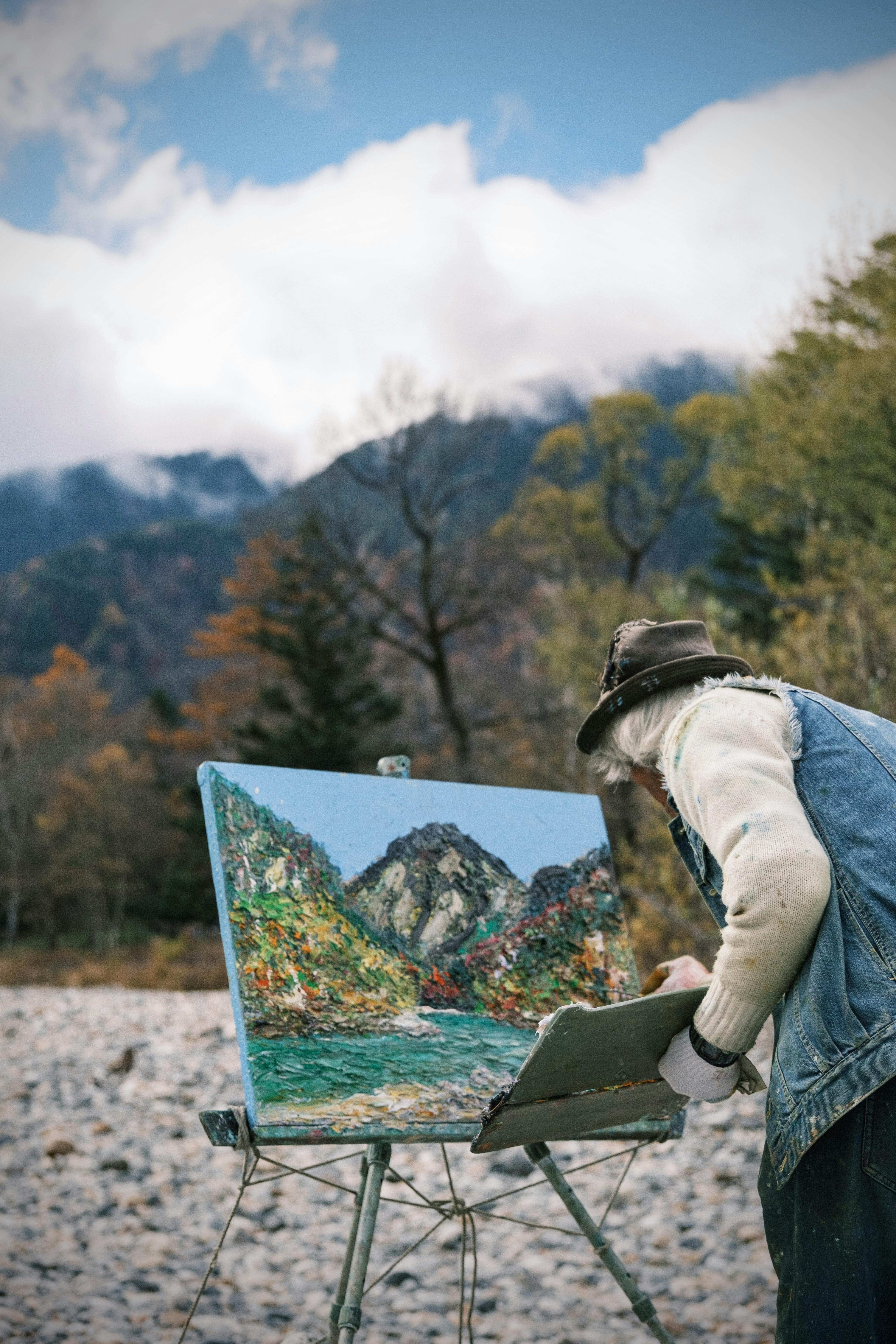Artist painting a mountain landscape en plein air, showcasing a portable easel.