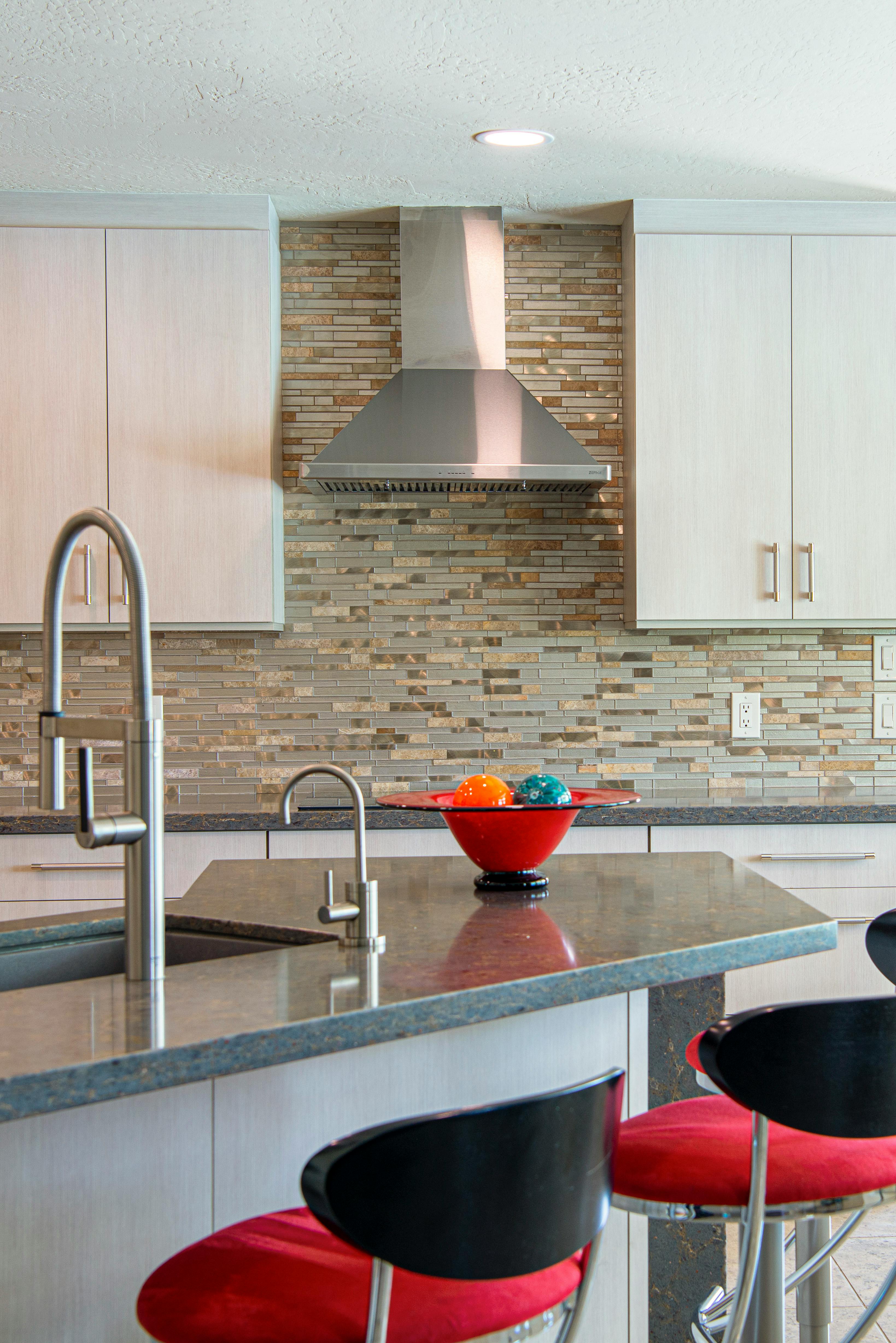 Modern kitchen with a decorative mosaic tile backsplash and a sleek stainless steel range hood.