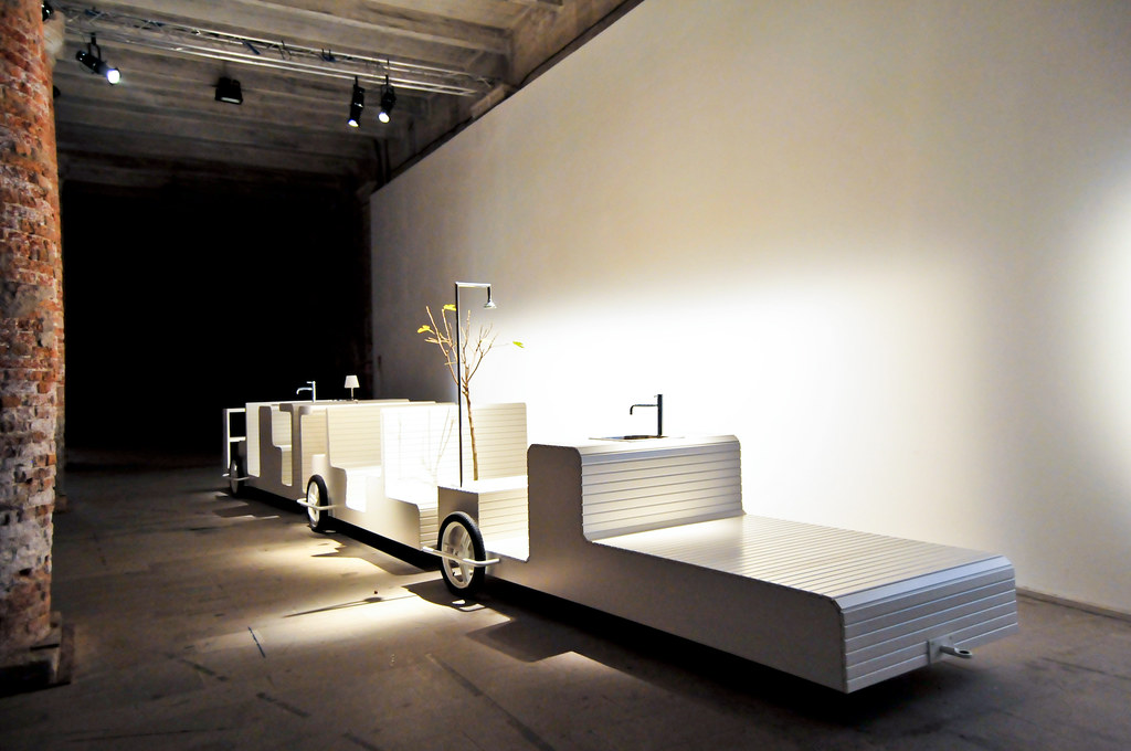 Venice Architecture Biennale 08 installation featuring a modular white structure resembling a train with sinks, lamps, and a decorative tree.