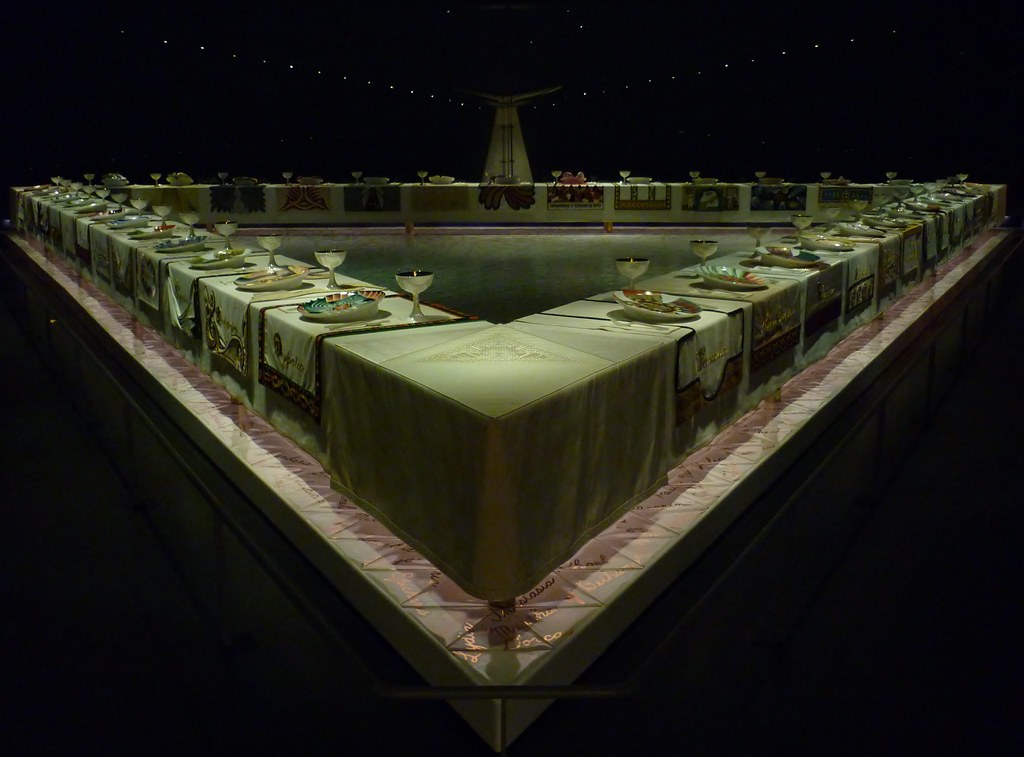 Judy Chicago's The Dinner Party installation at the Brooklyn Museum, featuring a triangular table with elaborate place settings.