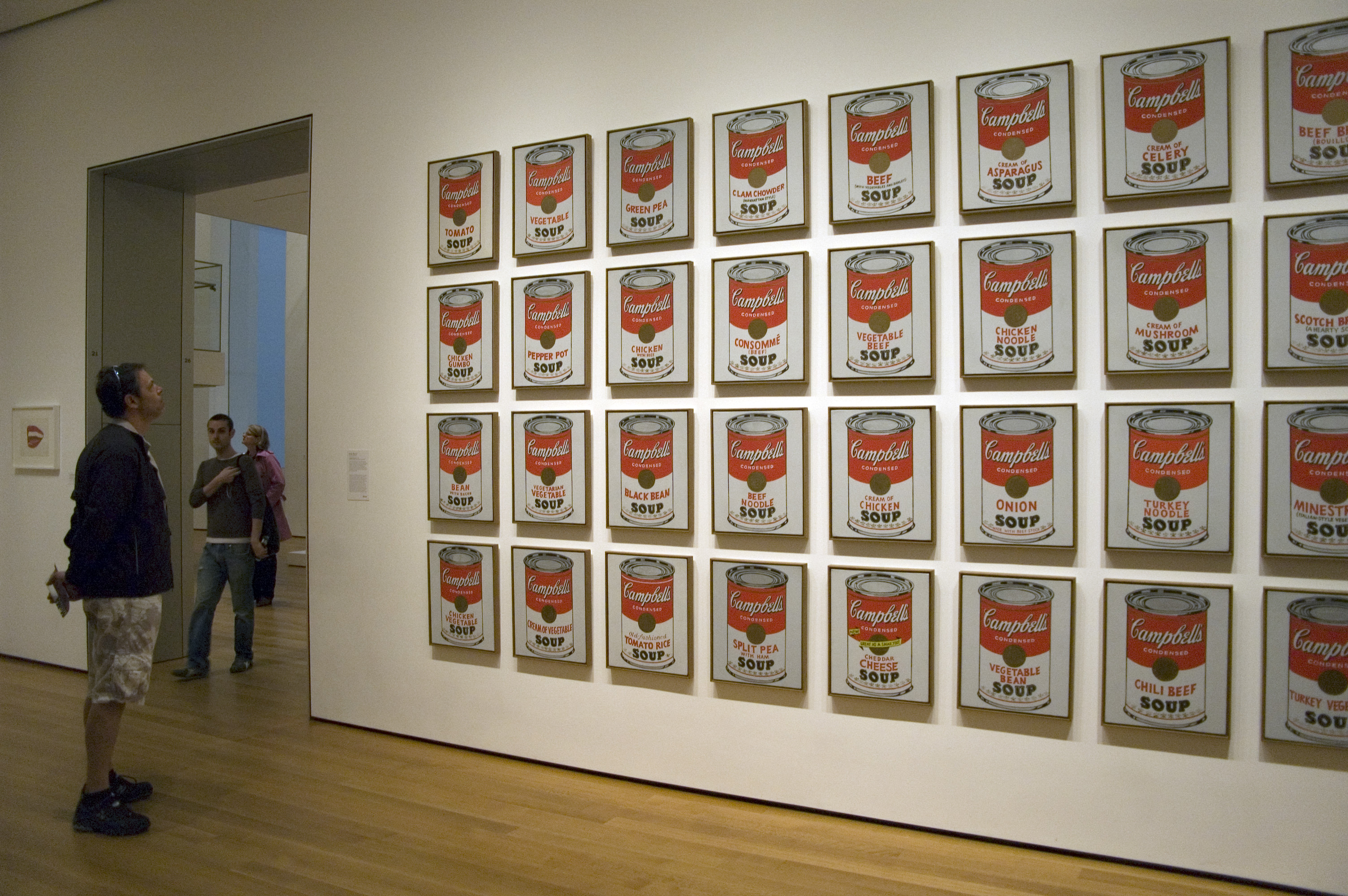 Andy Warhol's Campbell's Soup Cans artwork displayed in a museum gallery with visitors observing.