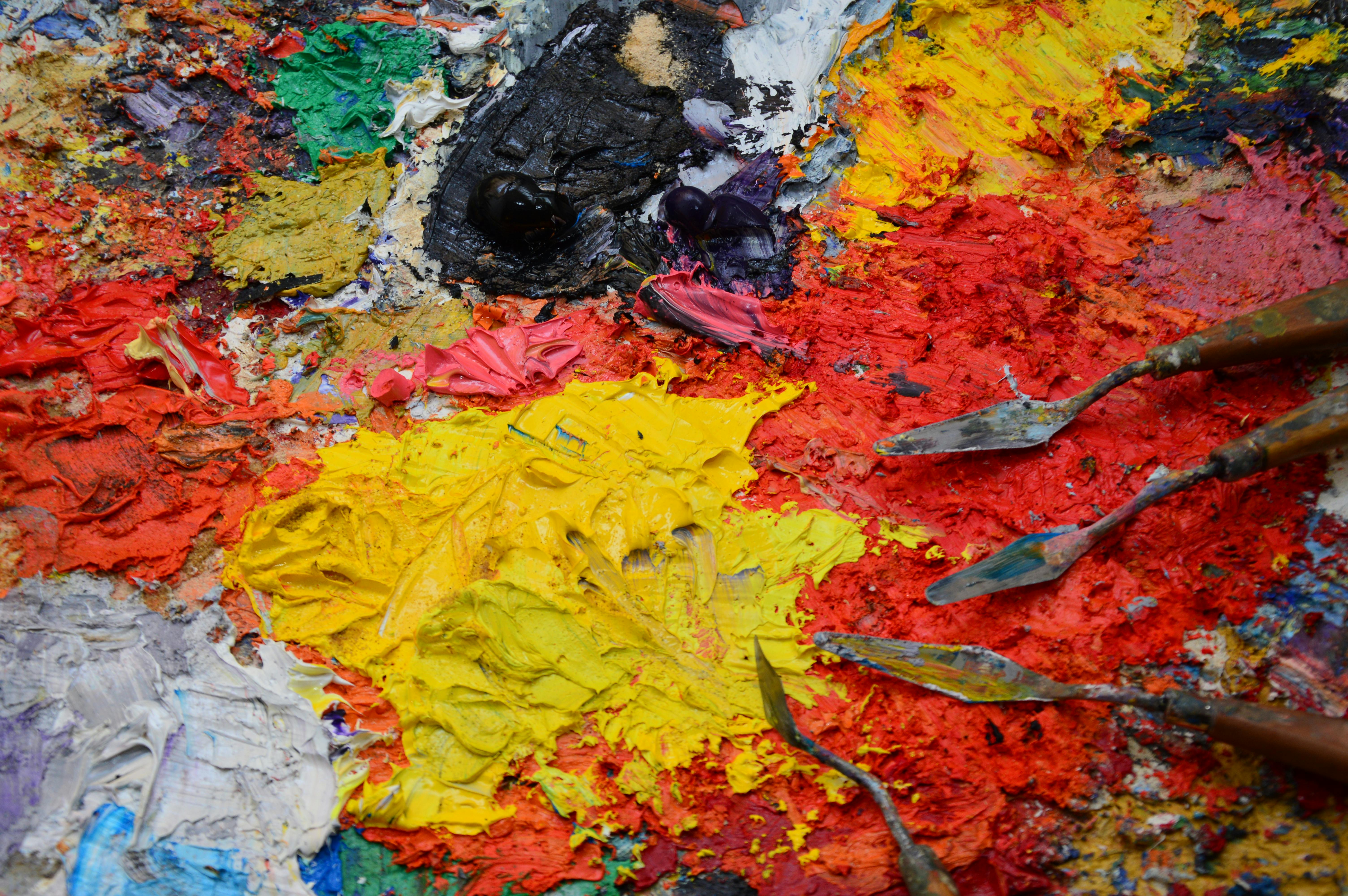 Close-up of a painter's palette covered in thick, vibrant oil paints and artfully arranged palette knives, showcasing rich textures and colors.