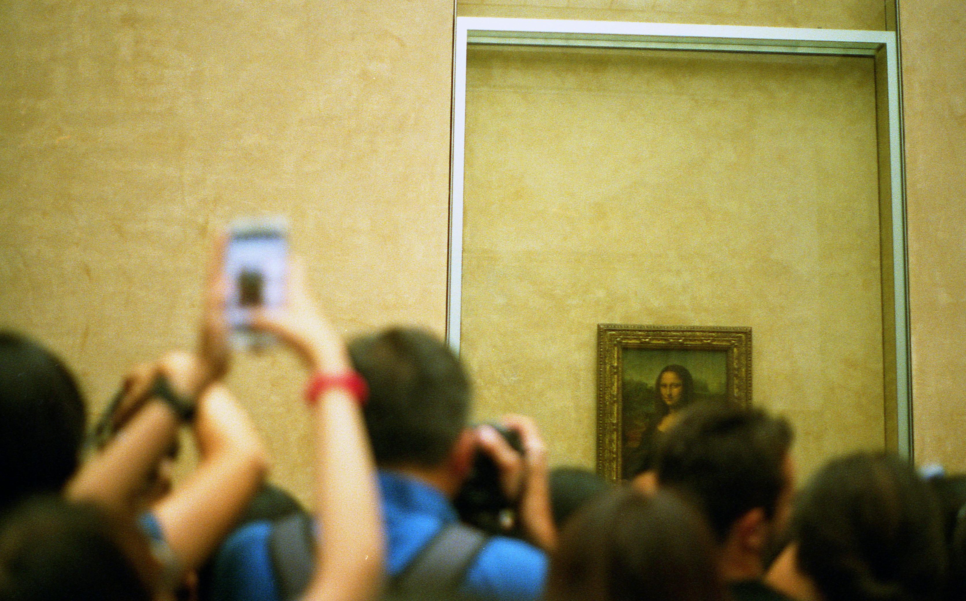 Group of people photographing the Mona Lisa in the Louvre museum, capturing the iconic artwork and its critical significance