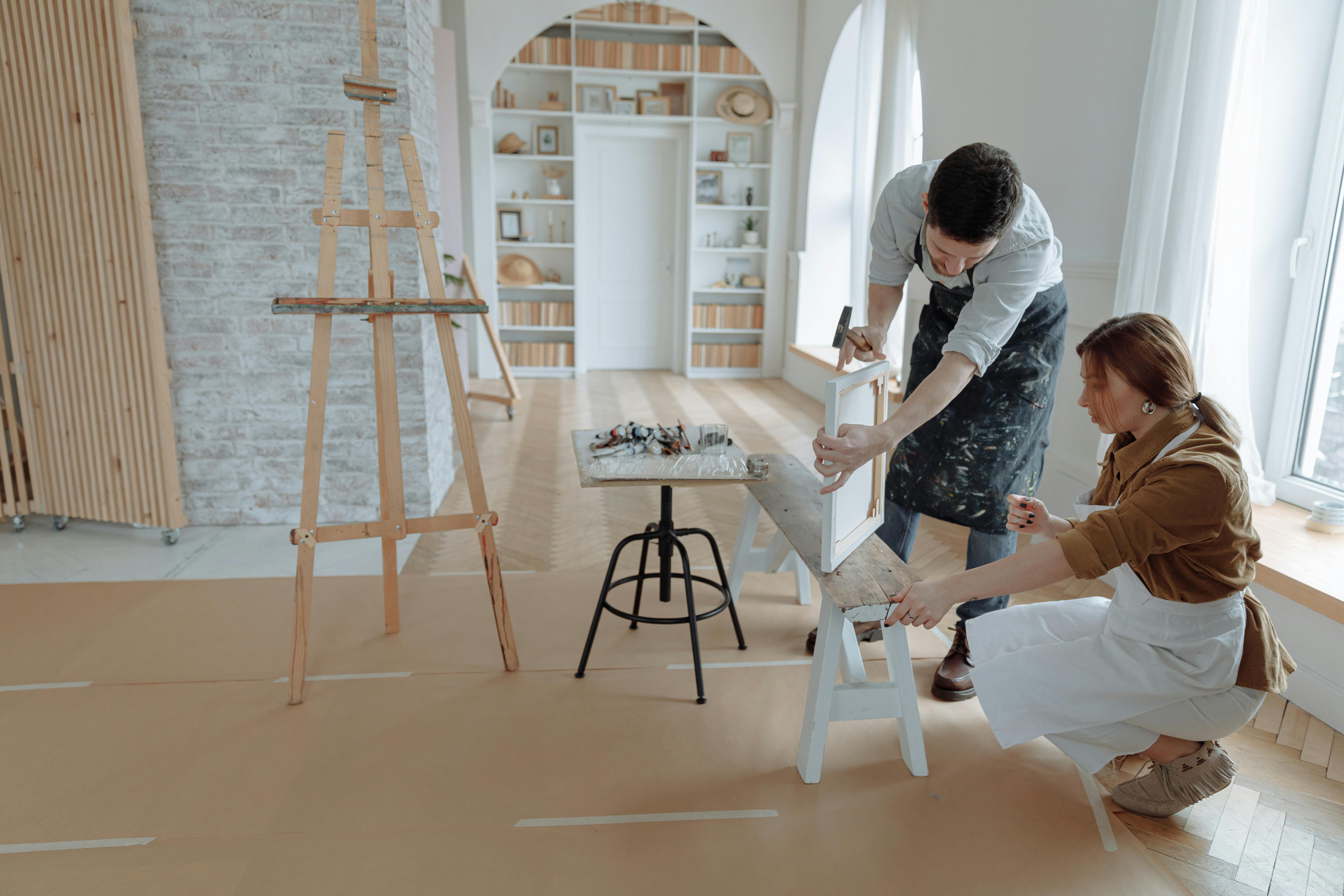 A man demonstrates how to frame a canvas to a woman in an art studio.