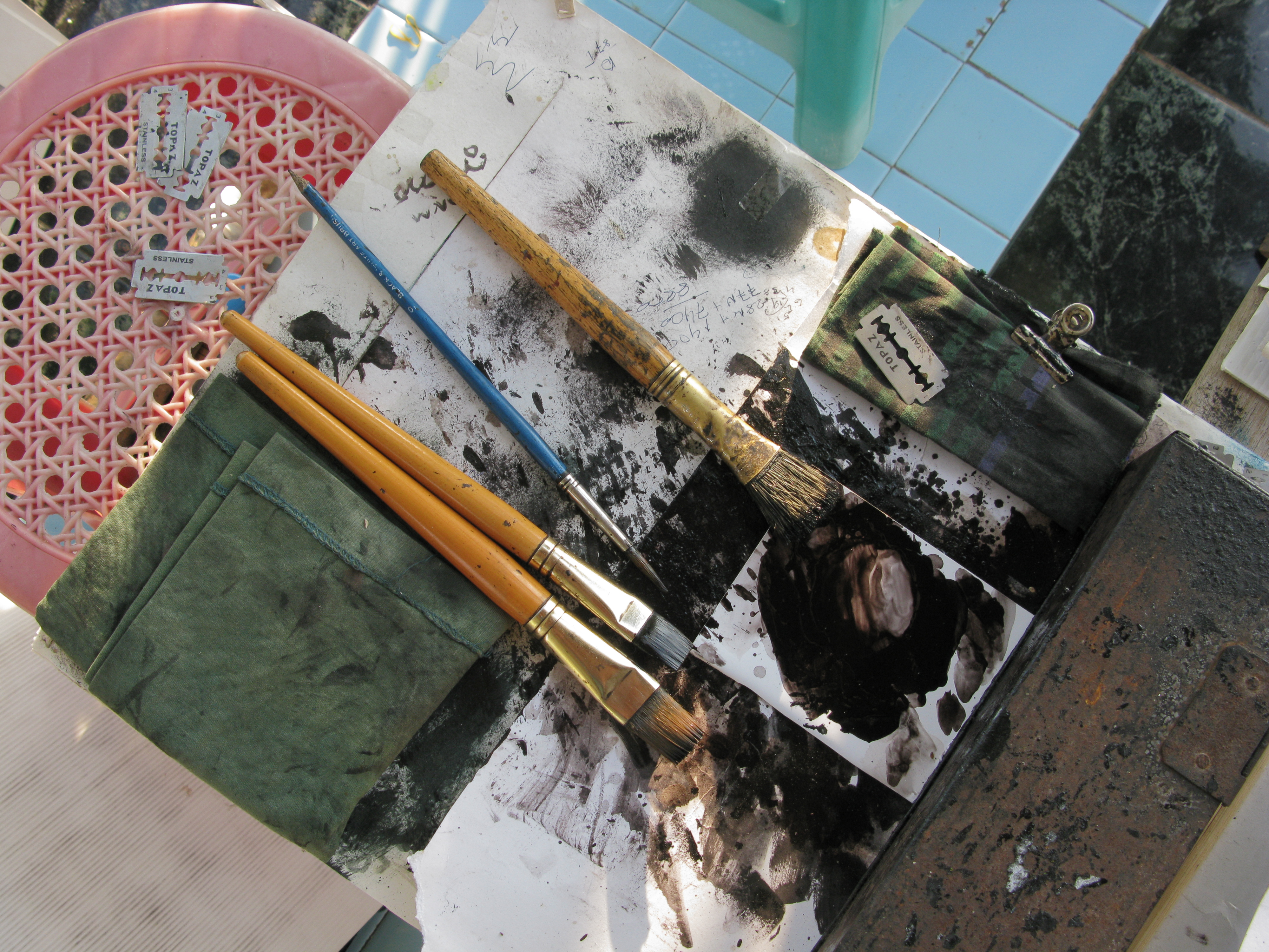Artist paint brushes and art supplies on a table in Sagaing, Myanmar, with paint stains and razor blades.