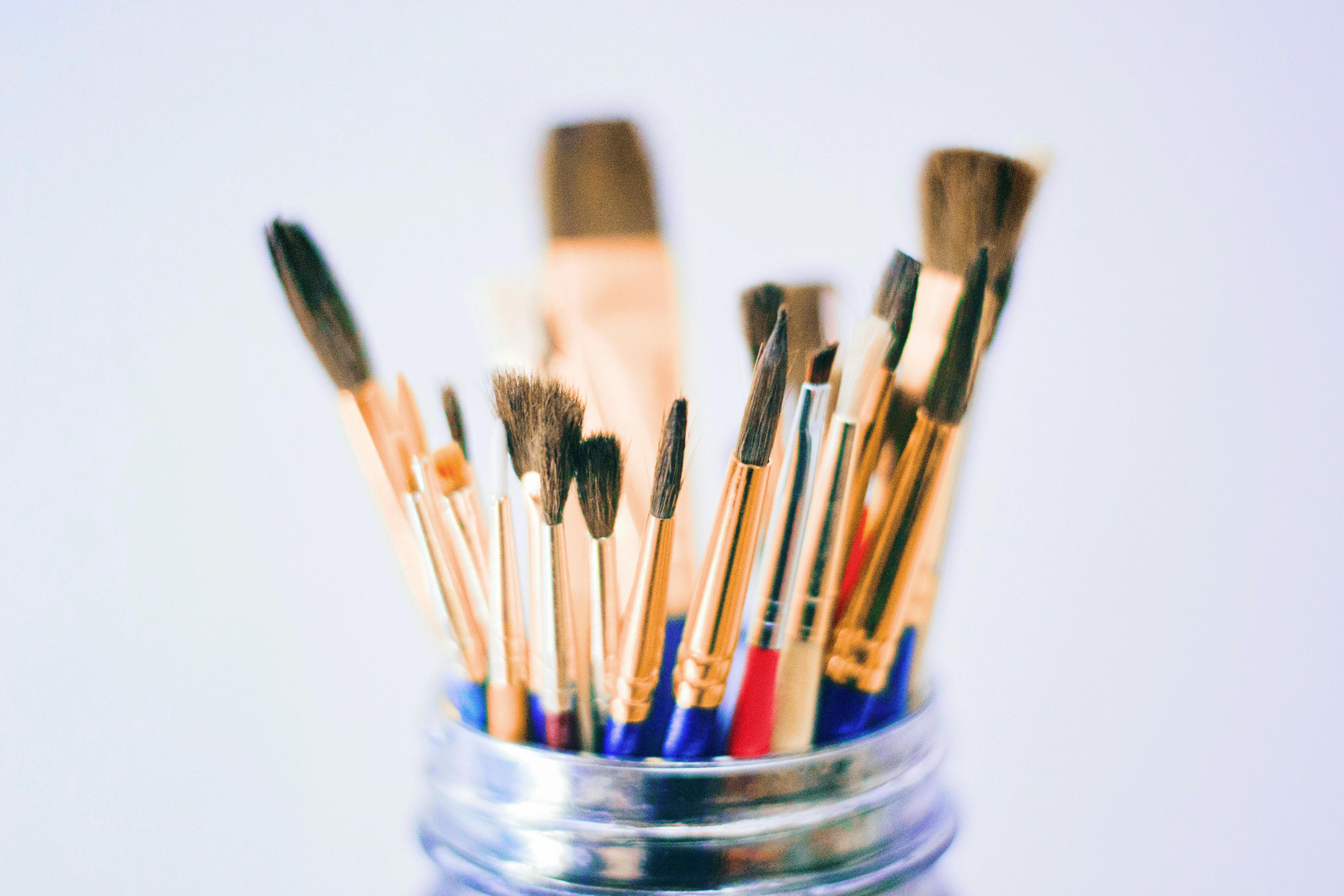 Shallow photography of various paint brushes in a jar with a metal rim, some with blue and red handles.