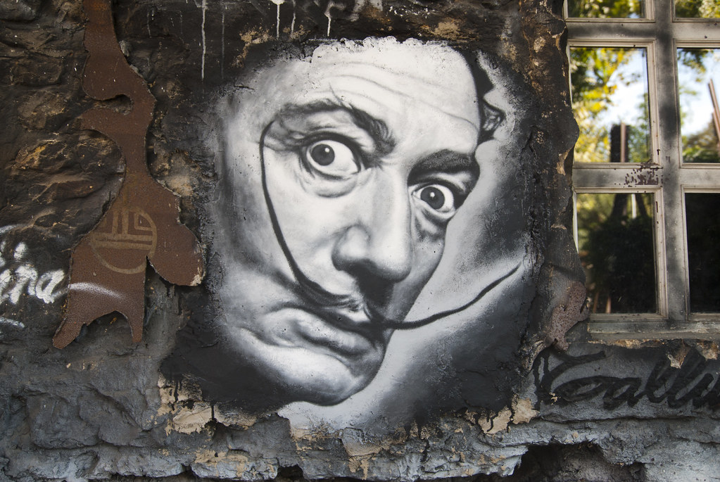Graffiti portrait of Salvador Dalí on a textured wall, featuring his iconic mustache and intense gaze.