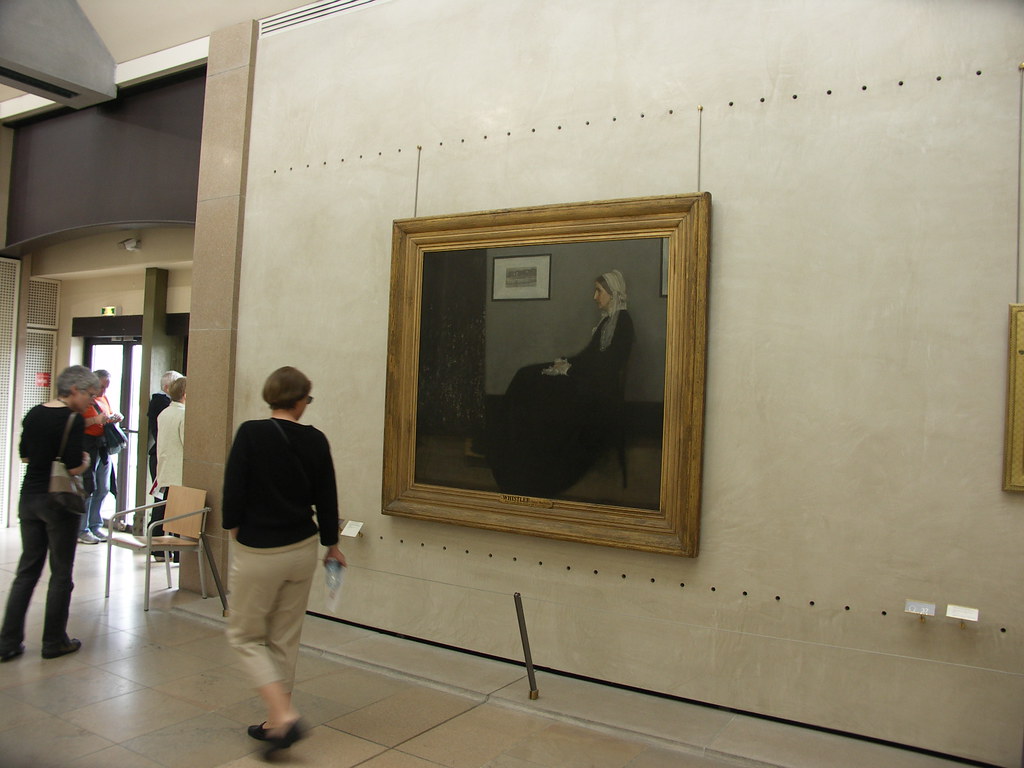 Whistler's Mother painting displayed at the Orsay Museum in Paris, with visitors in the foreground.