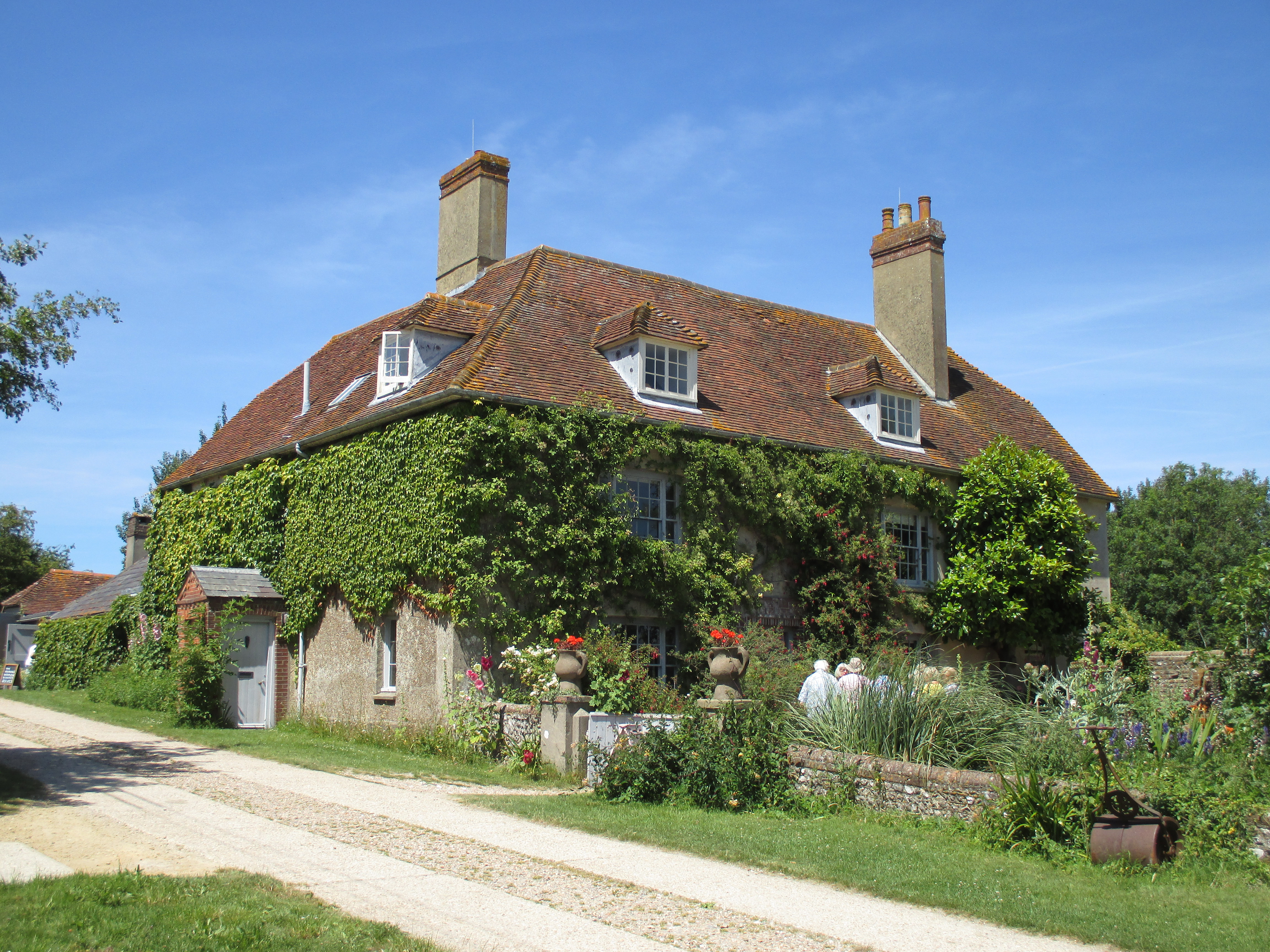 Charleston farmhouse, former home of the Bloomsbury Group artists Vanessa Bell and Duncan Grant, covered in ivy with a garden and blue sky.