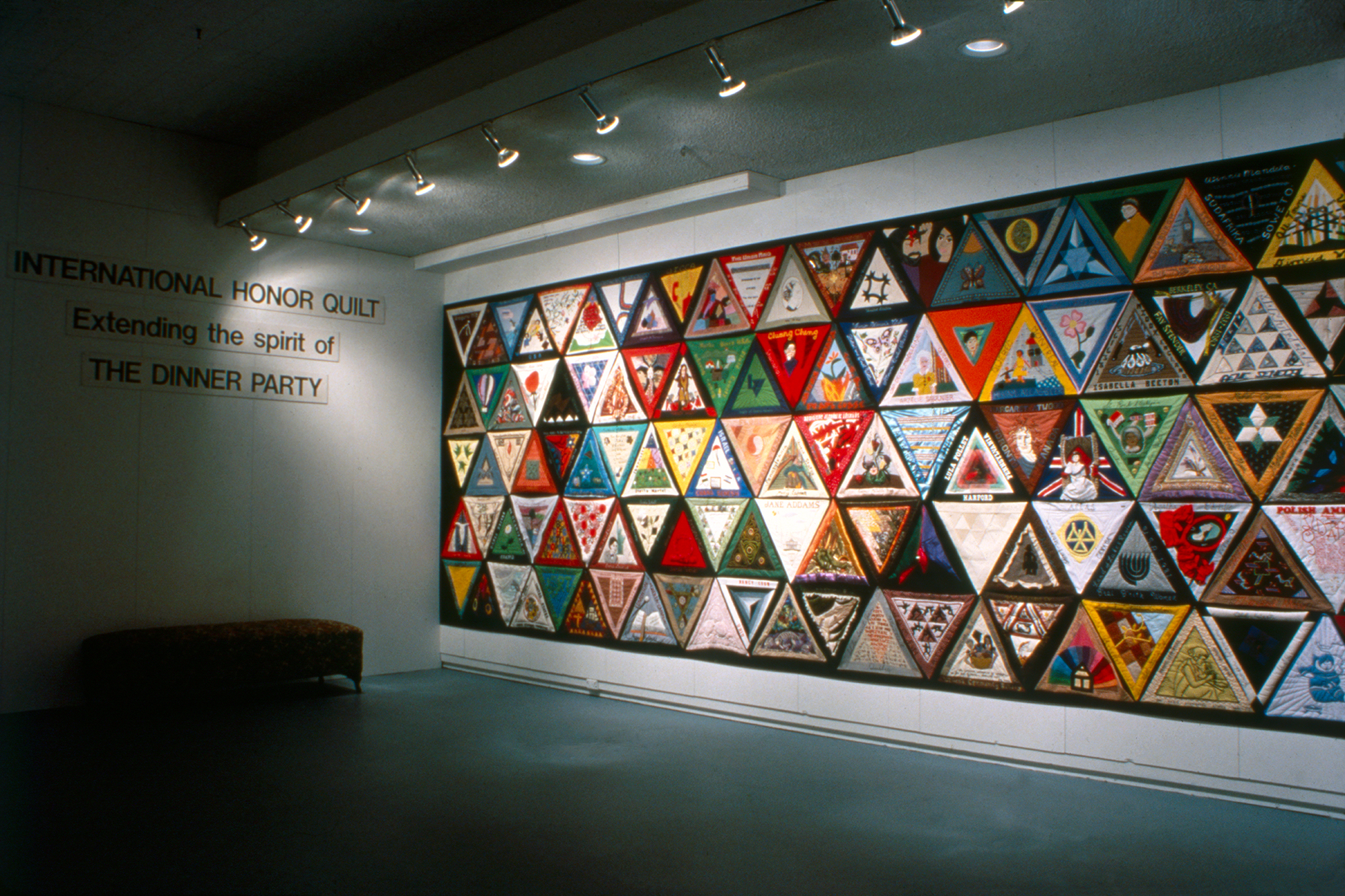 The International Honor Quilt, a large triangular quilt extending the spirit of Judy Chicago's The Dinner Party, displayed on a gallery wall.