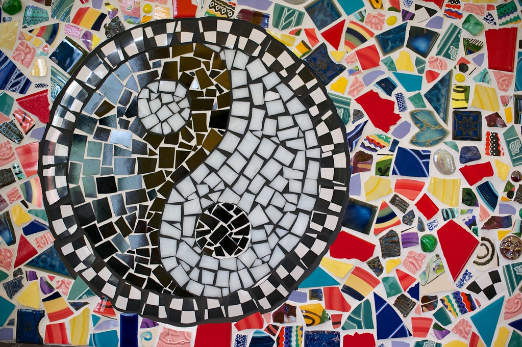 Abstract Yin Yang mosaic art displayed on a fireplace mantel, featuring colorful broken tile fragments surrounding a black and white yin yang symbol.