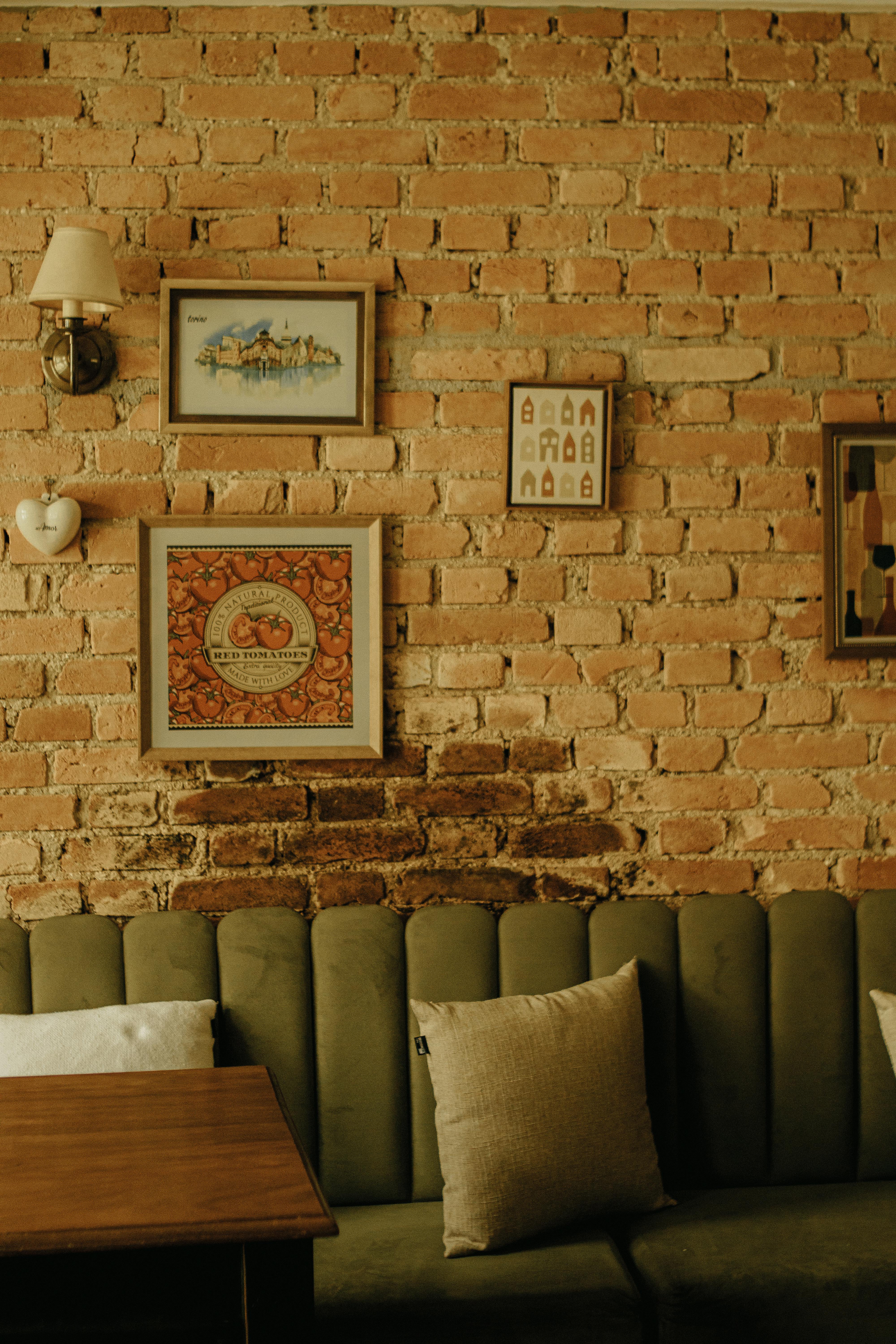 Cozy vintage cafe interior with a green velvet sofa, wooden table, and brick wall decorated with framed art and a heart-shaped ornament.