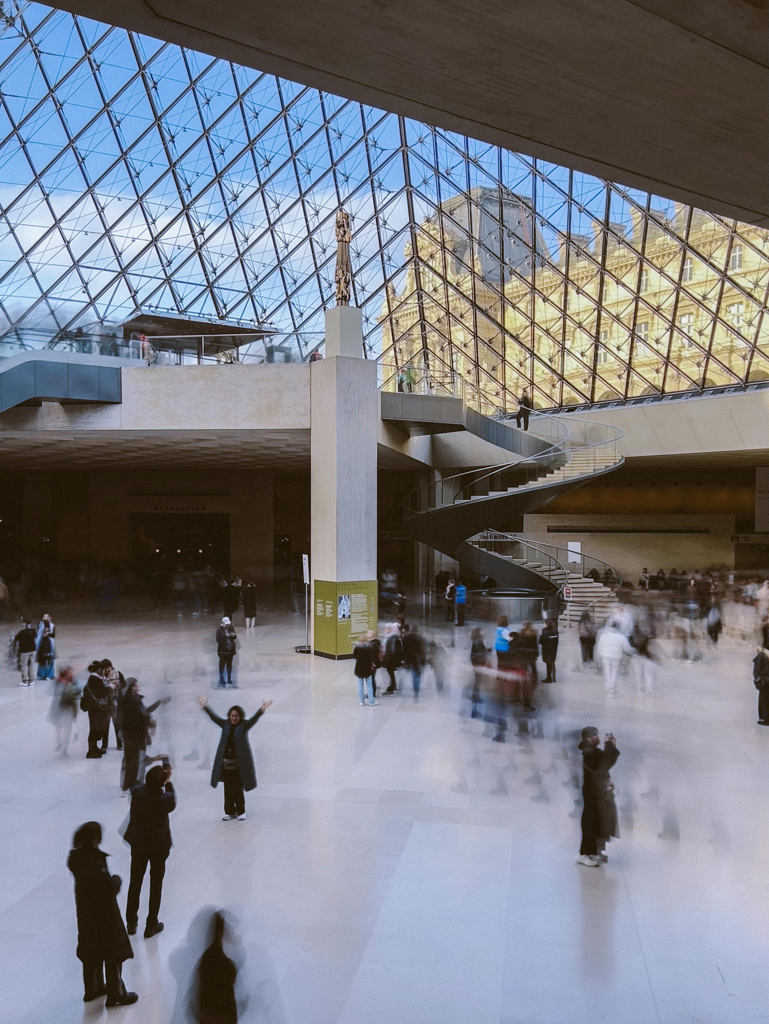 Bustling interior of the Louvre Pyramid with tourists and architectural details