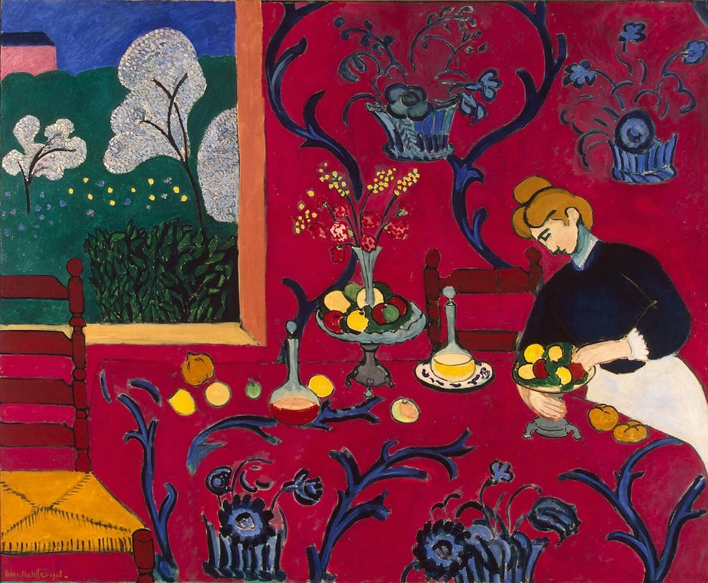 Henri Matisse's 'The Red Room' (Harmony in Red), a vibrant painting featuring a woman arranging fruit on a red table with blue floral patterns, next to a window overlooking a green landscape.