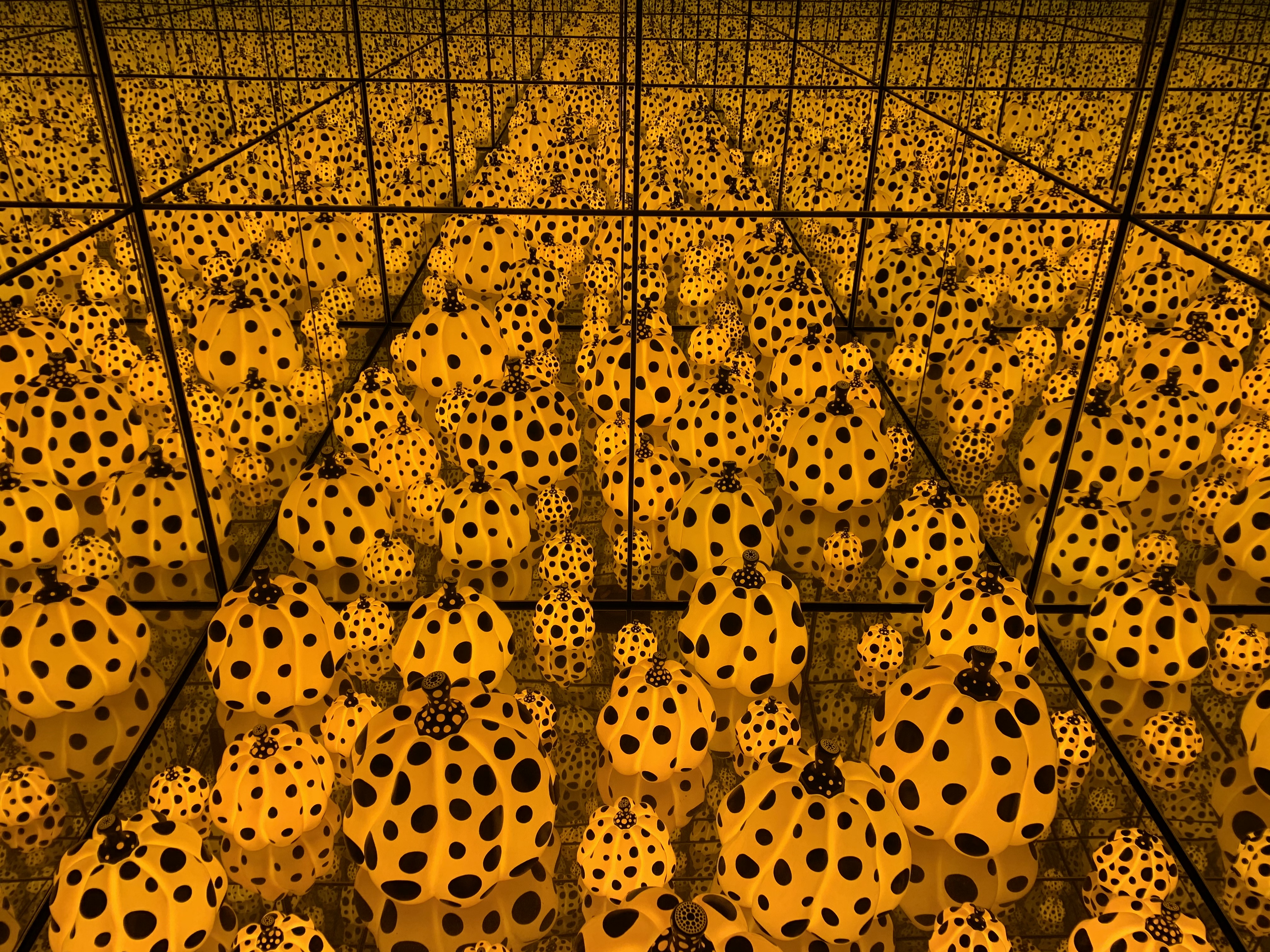 Yayoi Kusama's 'Infinity Mirrored Room' filled with countless yellow pumpkins covered in black polka dots, creating an endless reflection.
