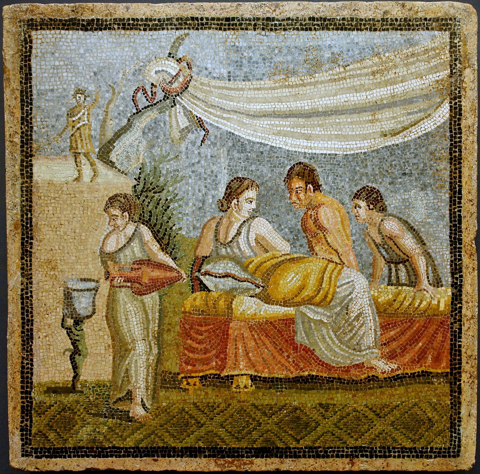 Roman mosaic depicting a love scene with figures reclining on a bed, a servant pouring wine, and a chariot in the background.