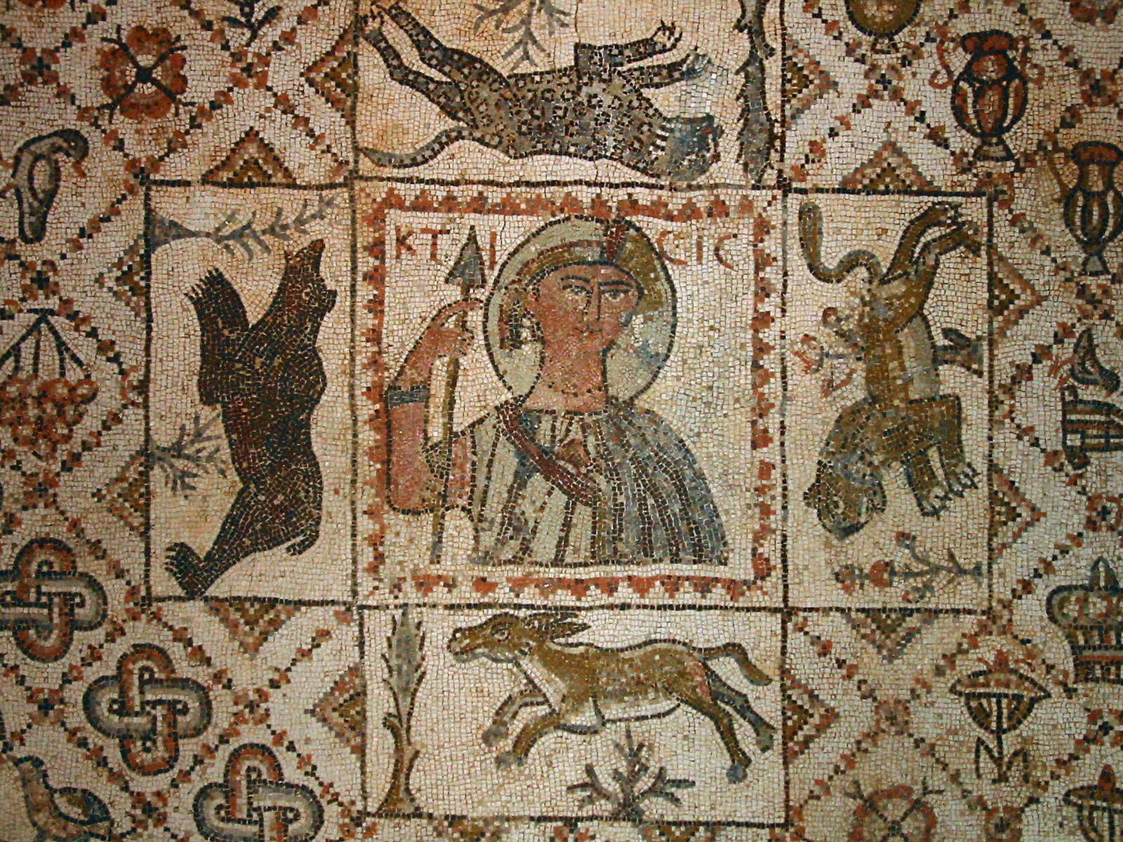 Byzantine mosaic depicting a central figure with a halo, holding a spear, surrounded by various animals and decorative elements. The inscription KTICIC is visible.