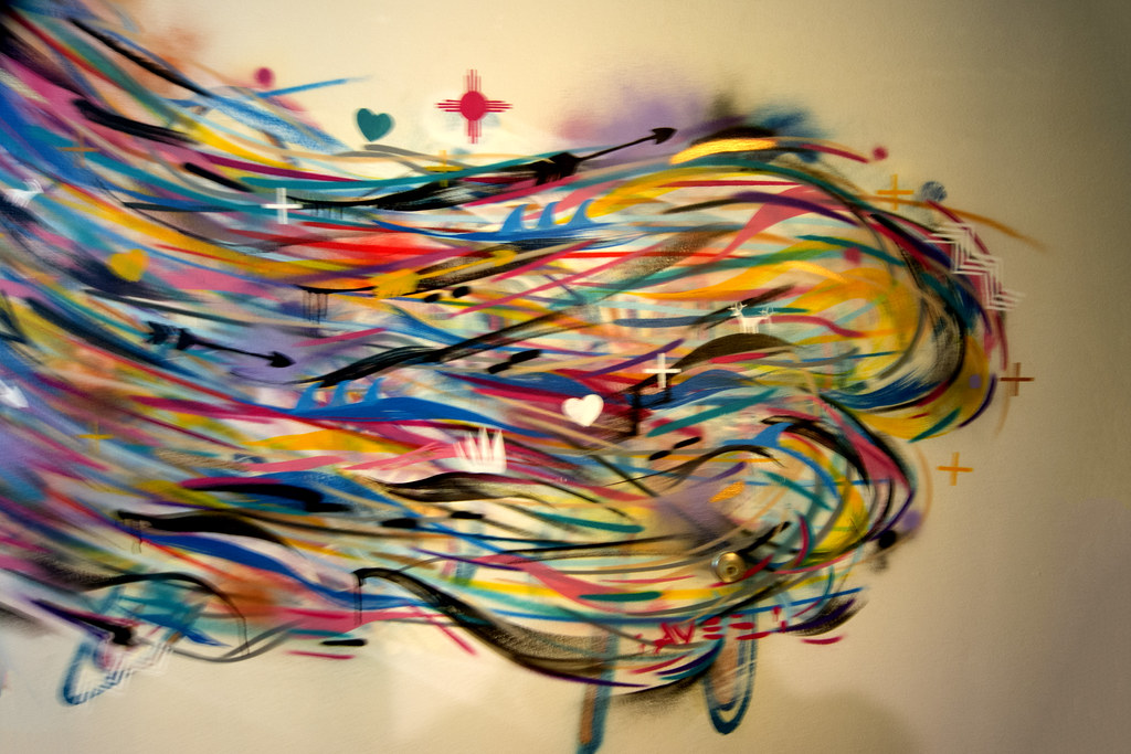 Vibrant abstract artwork with colorful swirling lines and symbolic elements like hearts, arrows, and crosses, titled "Winds of Change" by Jay Smiley.