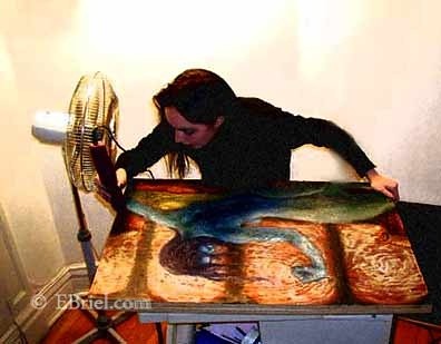 Artist working on an encaustic painting with a fan blowing on it.
